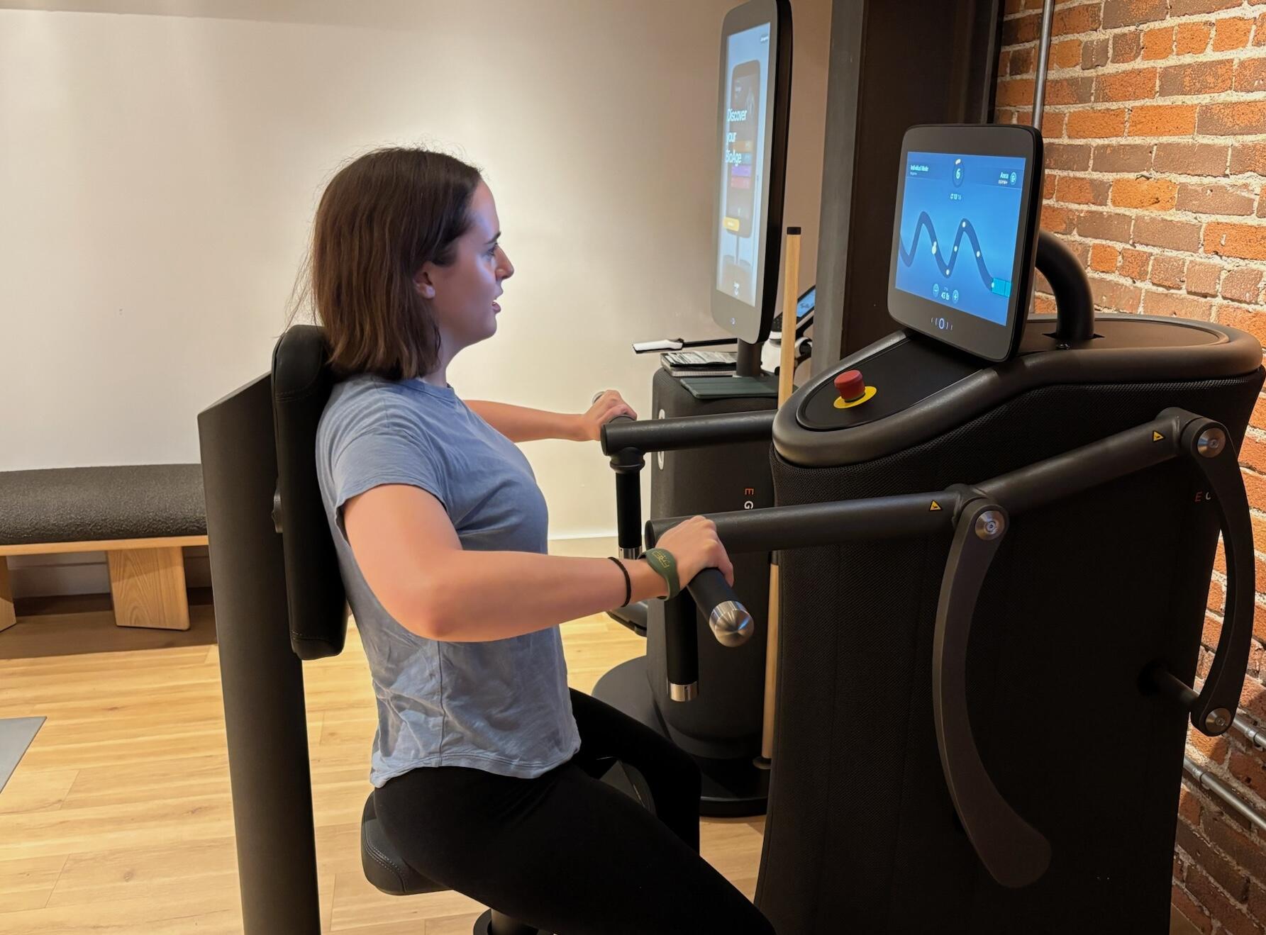 شخص بشعر بني قصير، يرتدي قميصًا أزرق وبنطلون ضيق أسود يلعب لعبة تشبه Pac-Man على جهاز تمرين الصدر.