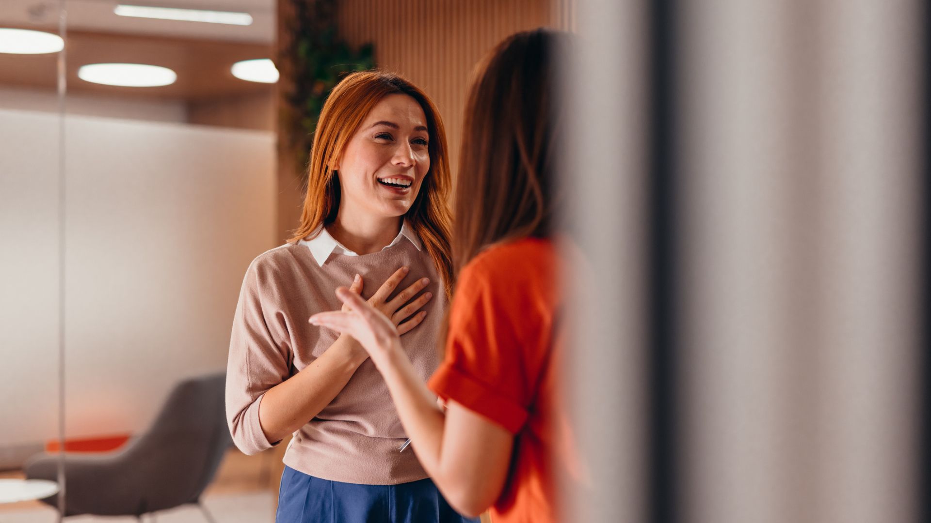 امرأة بشعر أحمر تبتسم وتضحك أثناء التواصل مع زميلها