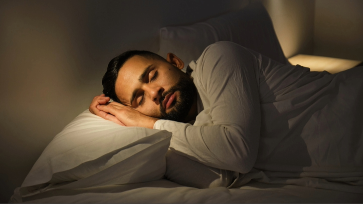 رجل نائم على جانبه في سرير بأغطية بيضاء وملابس نوم بيضاء