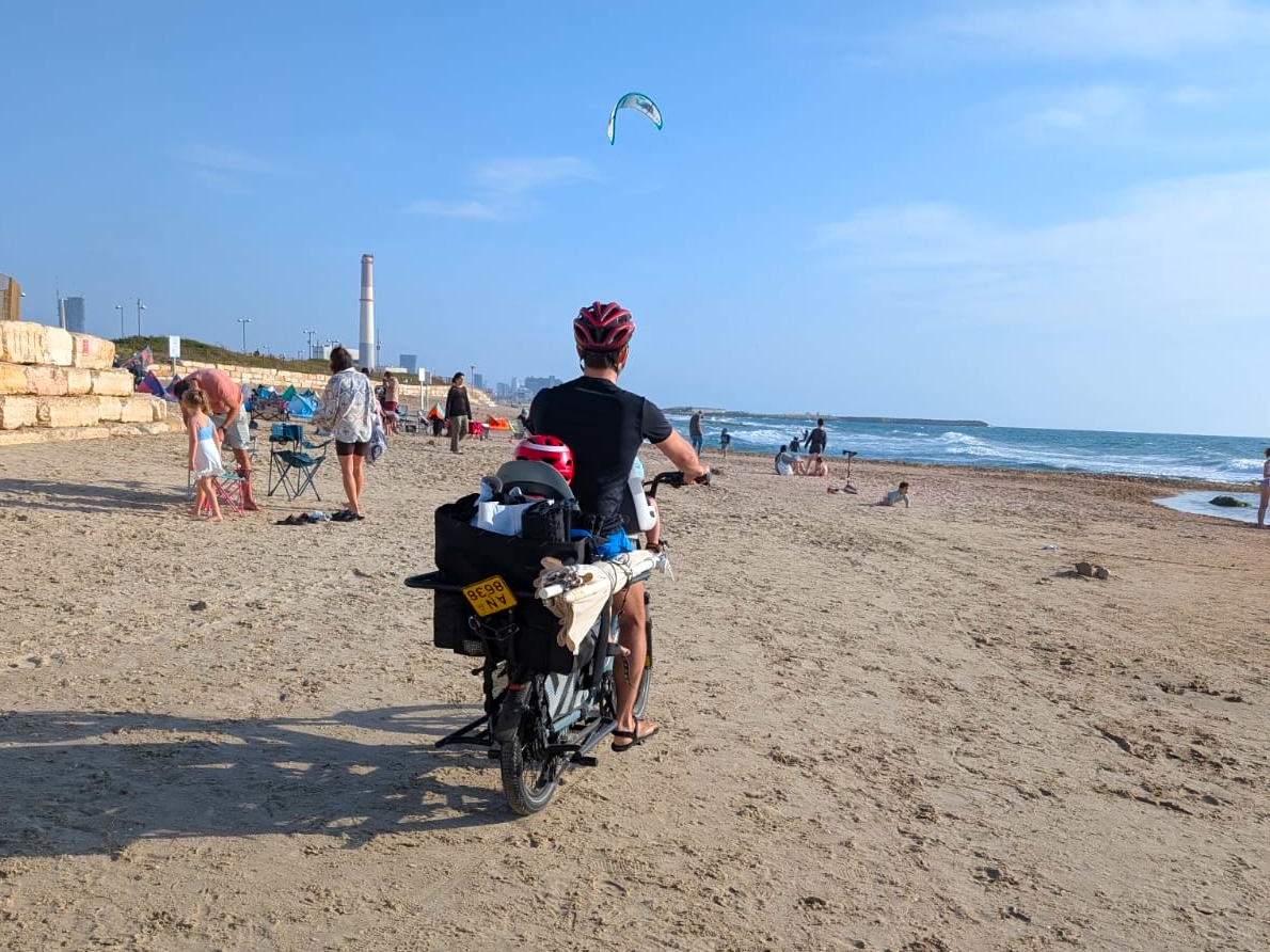 صورة لدراجة شحن كهربائية عائلية من طراز Xtracycle Family Hopper 2، وعليها طفلان يجلسان في المقعد الخلفي، مع شخص بالغ يقود الدراجة.