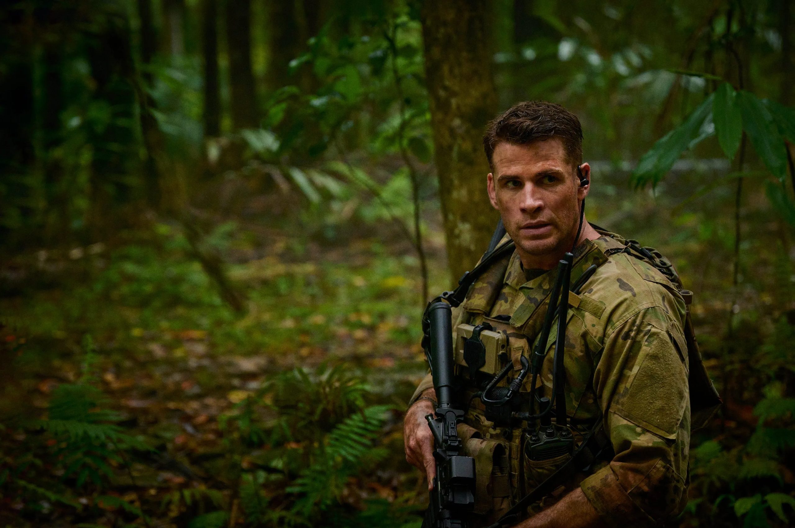 Liam Hemsworth holds a gun and stares.