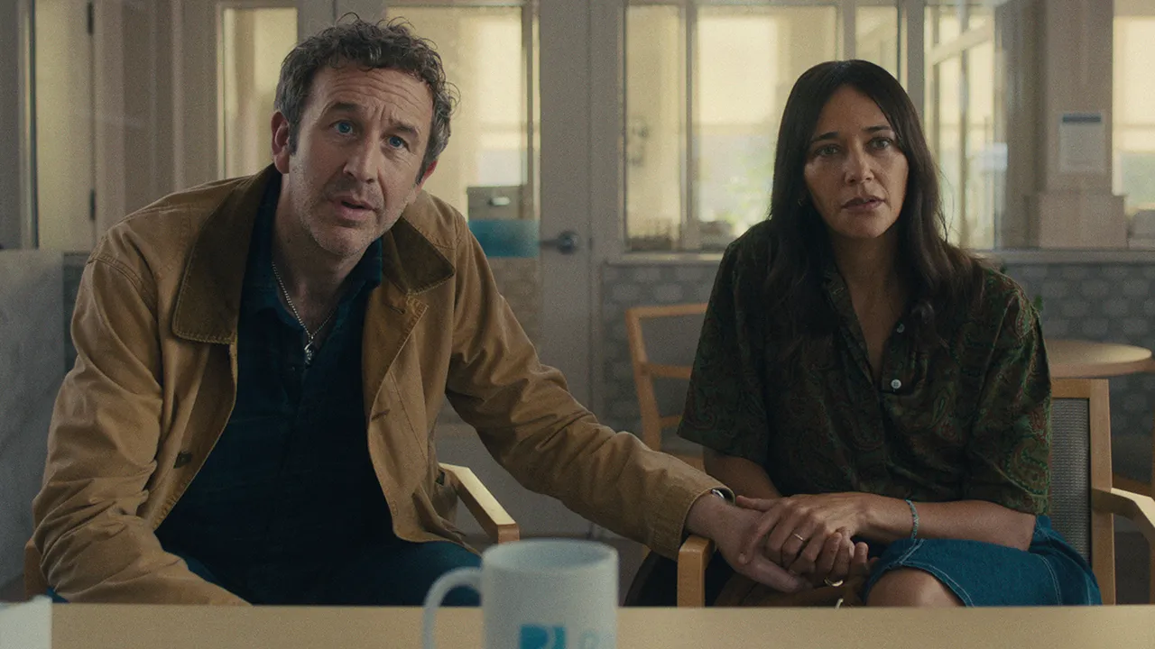 A man holds a woman's hand as they talk to someone across the table in the Common People episode of Black Mirror.