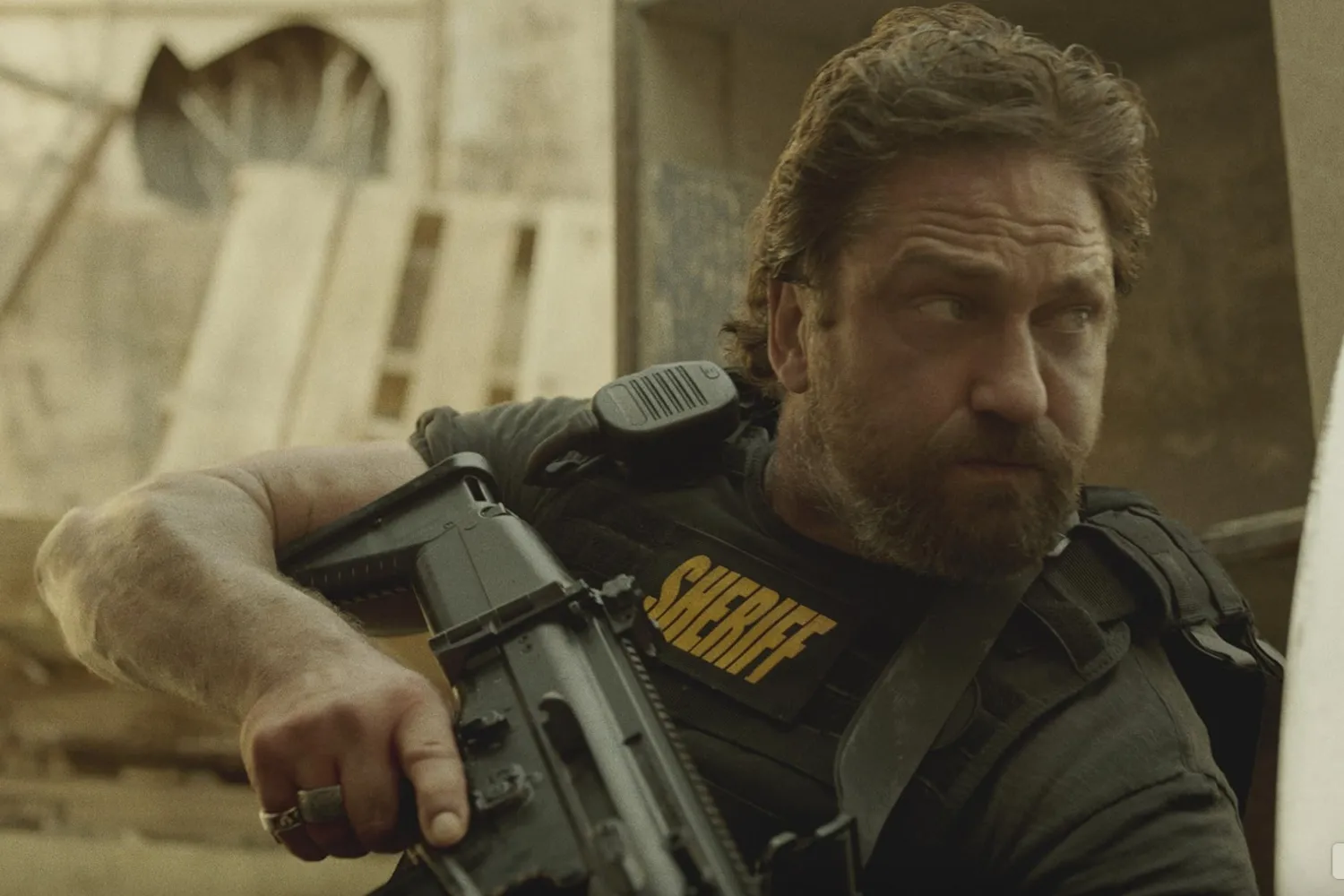 Gerard Butler holds a gun and stares intently.