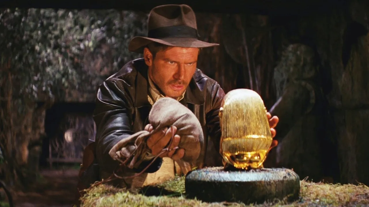 Indiana Jones looking at a statue intently while holding a bag in one hand in "Raiders of the Lost Ark."
