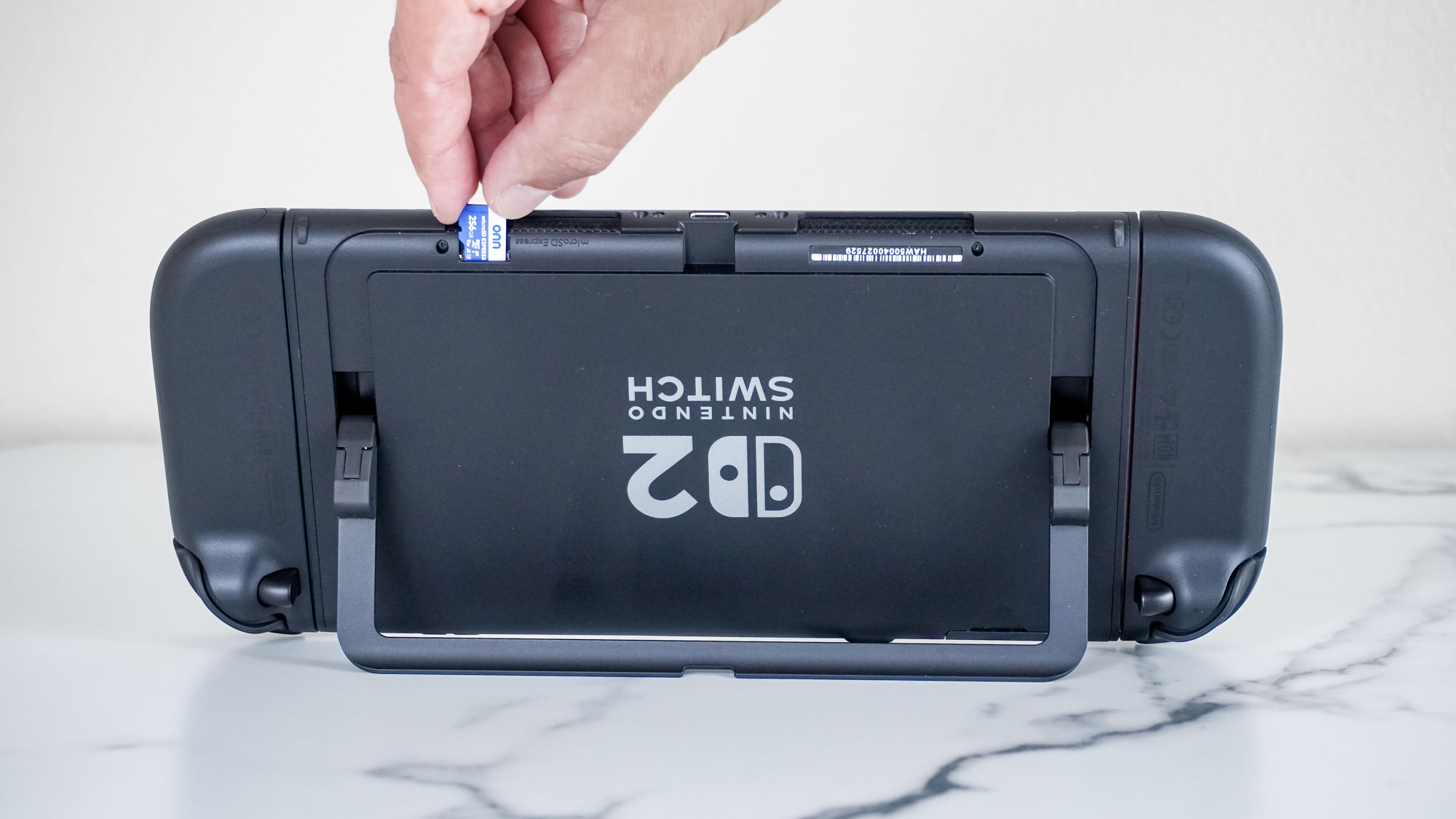إدخال بطاقة microSD Express في جهاز Switch 2 مع وضع الجهاز رأسًا على عقب على المكتب
