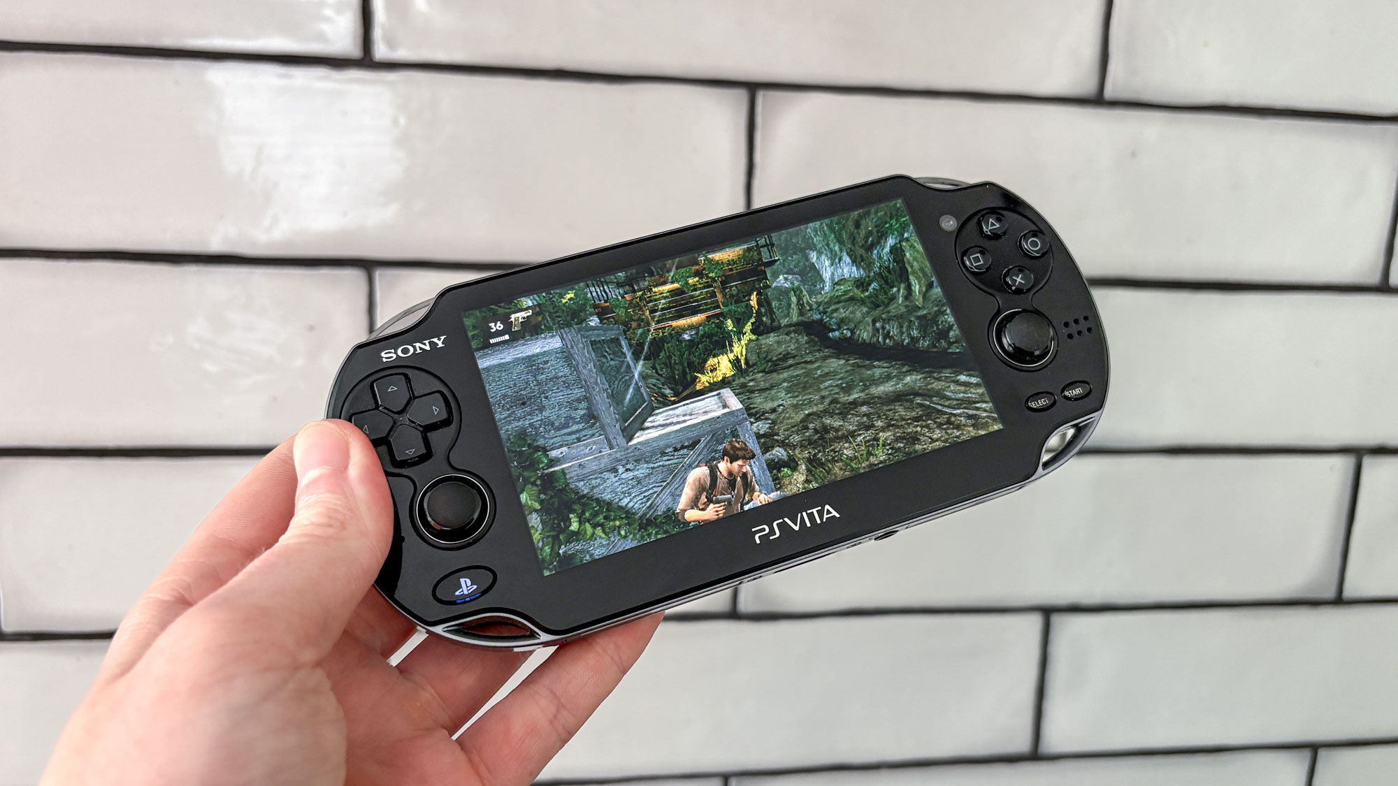 PS Vita head in hand with white tile background with Uncharted: Golden Abyss on display