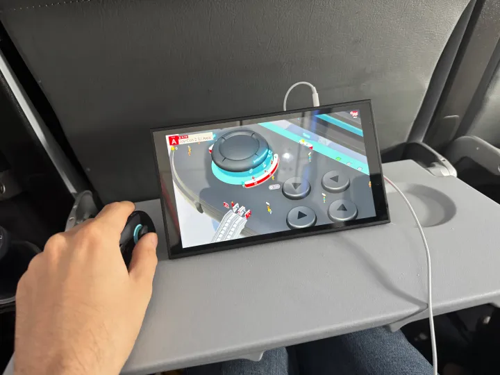 A hand holds a Joy-con like a mouse on an airplane tray table.