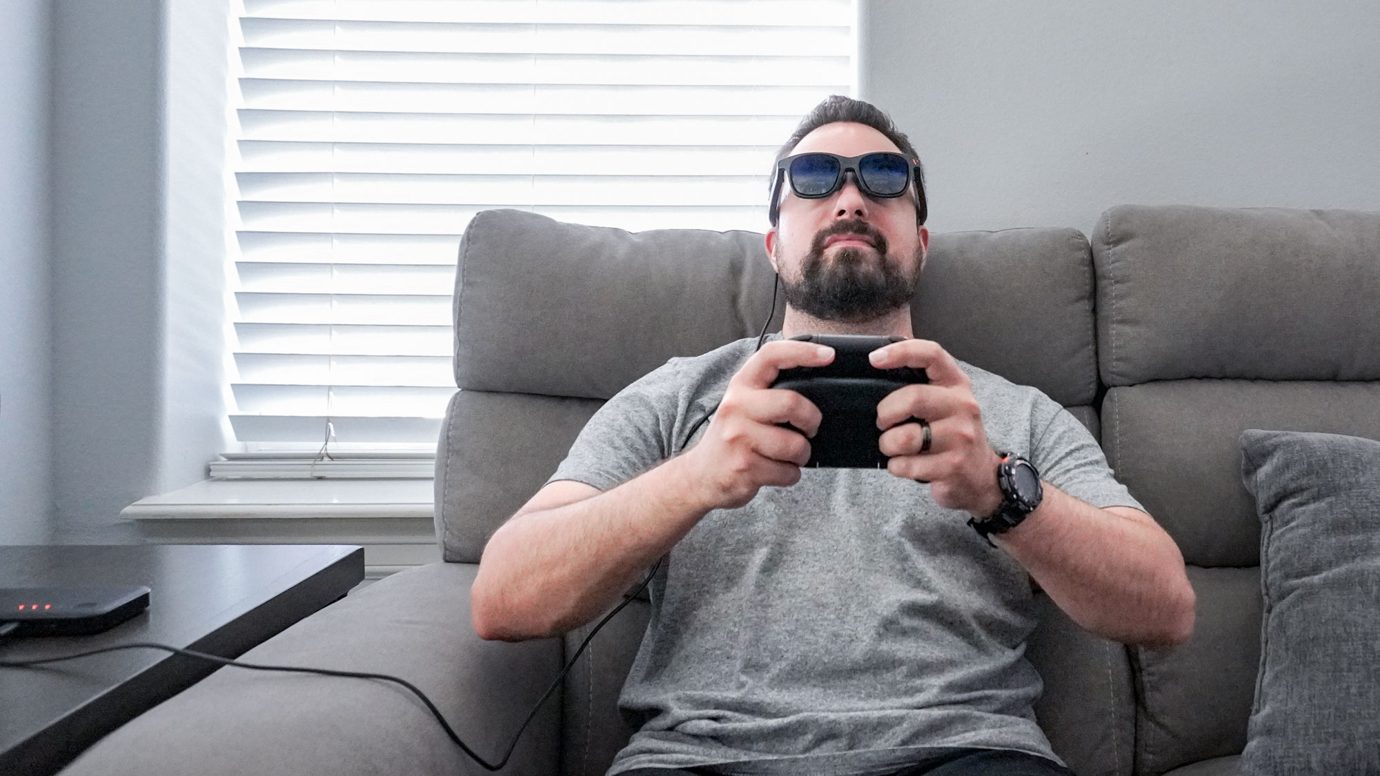 A person playing the Nintendo Switch 2 while wearing AR glasses on a couch using the Viture Pro Mobile Dock