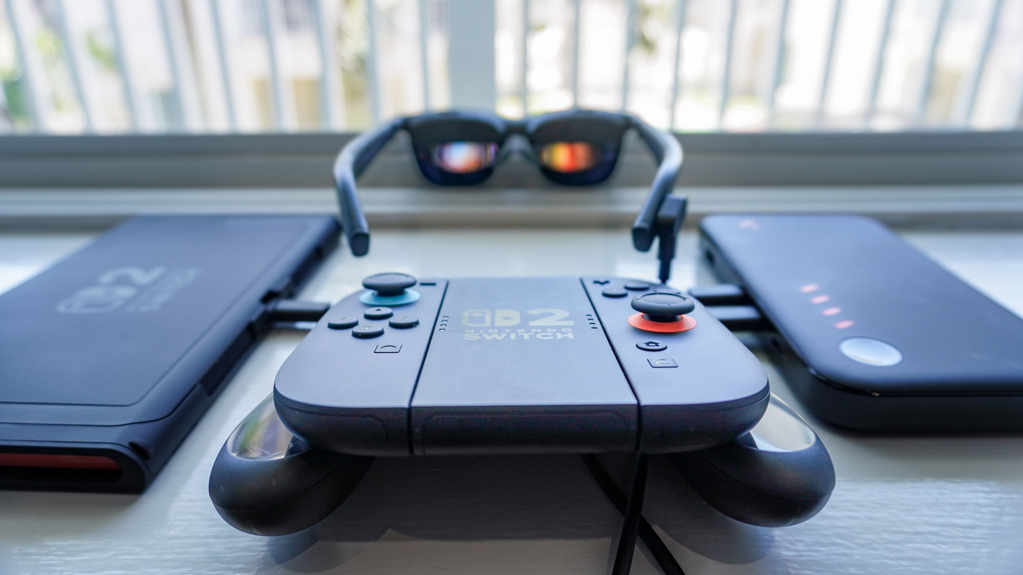 A Nintendo Switch 2 connected to the Viture Pro Mobile Dock with a controller in front and the Viture Pro XR glasses in the background