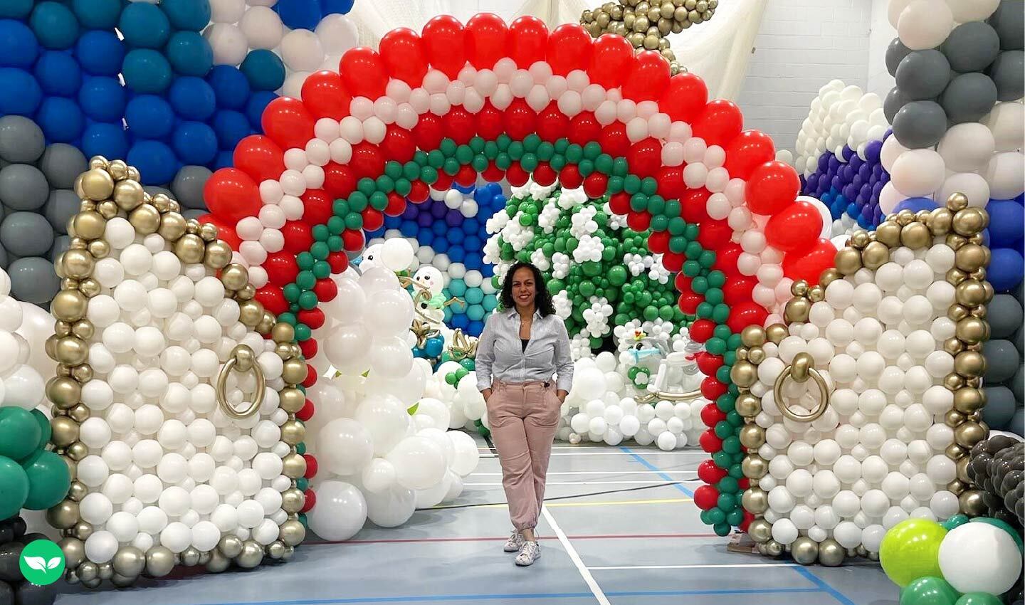 Karen Capelan si trova sotto un grande arco di palloncini color arcobaleno all'interno di una palestra, circondata da elaborate sculture di palloncini.