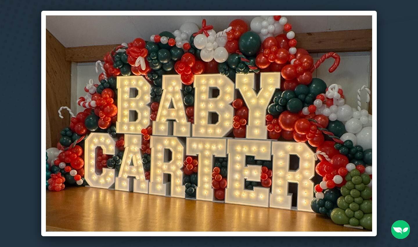Una vivace composizione di palloncini con lettere illuminate che formano la scritta "Baby Carter", con decorazioni natalizie nei colori rosso, verde e bianco.