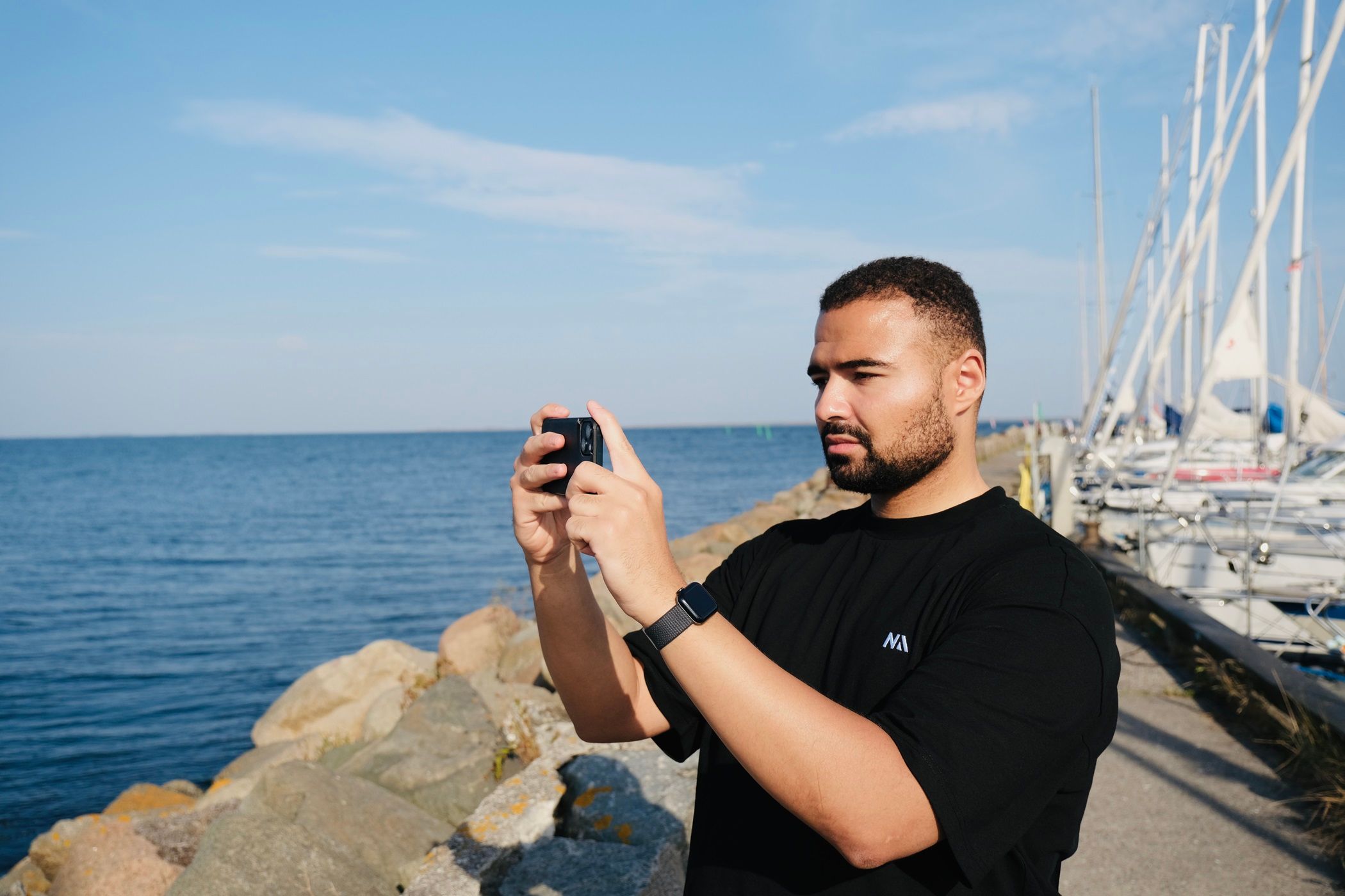 A man taking photos on their smartphone while standing next to the ocean