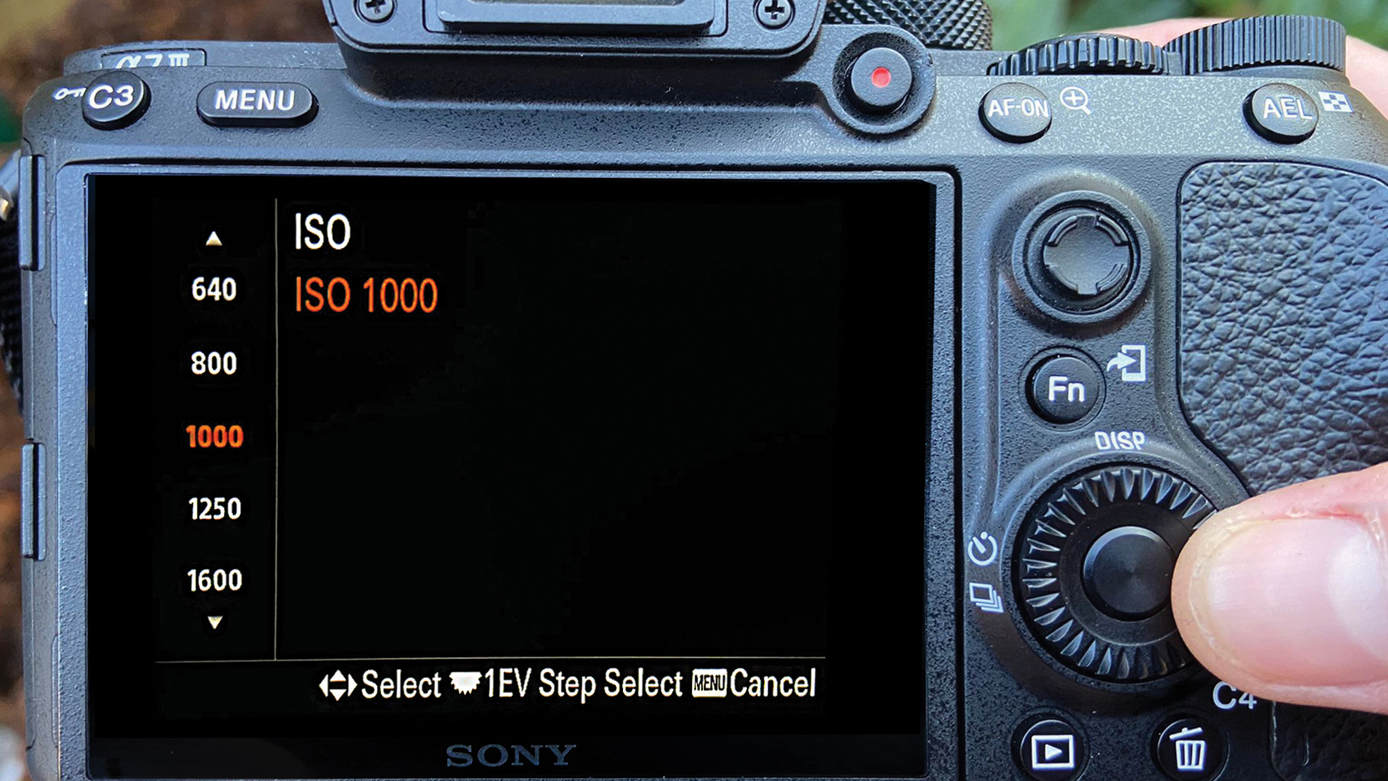 لقطة مقربة لشاشة كاميرا رقمية تعرض إعدادات ISO، مع تمييز ISO 1000 باللون الأحمر. يد تقوم بضبط القرص، مما يدل على الدقة والتحكم.
