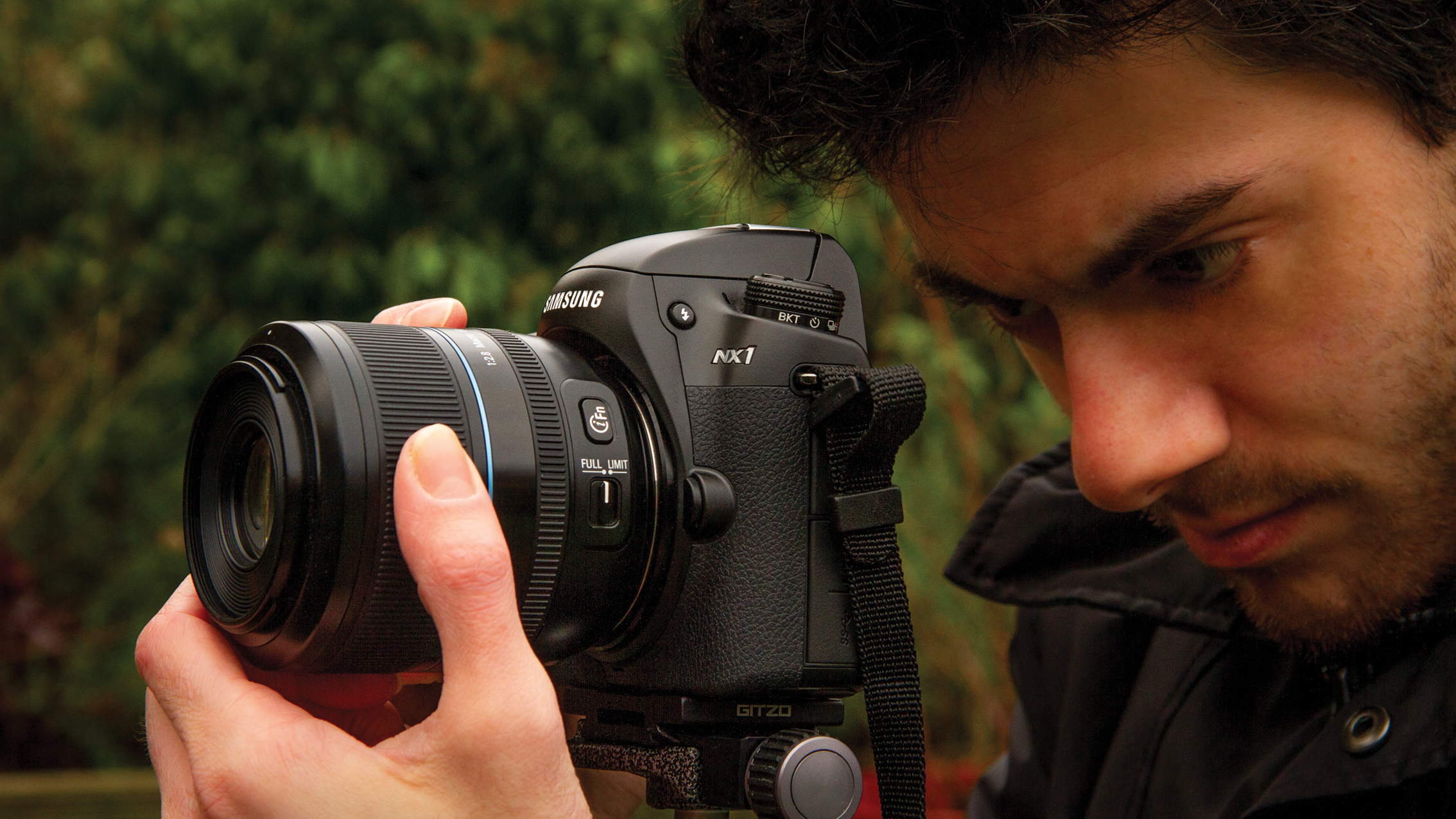 لقطة مقربة لرجل يضبط بعناية كاميرا Samsung NX1 بعدسة كبيرة في الهواء الطلق