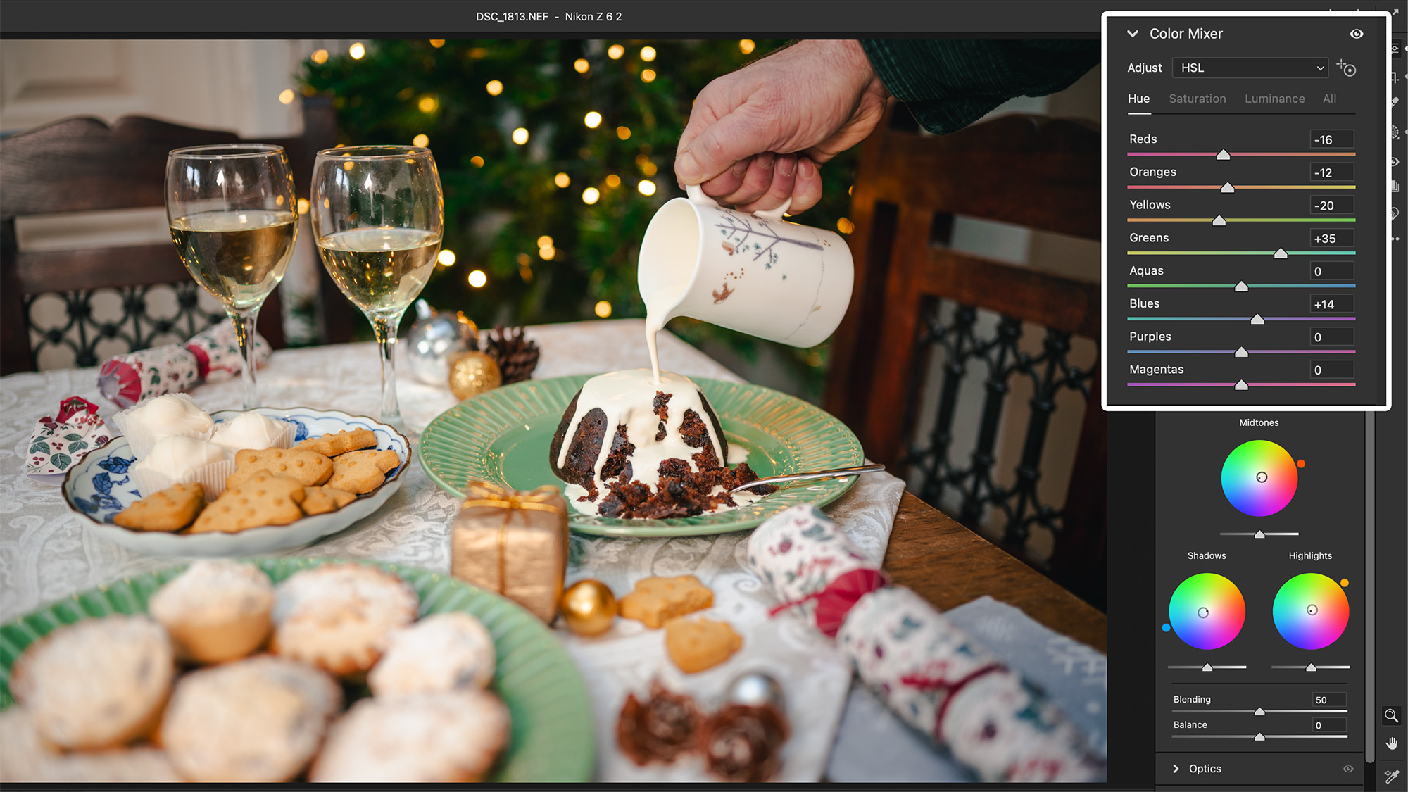 لقطة شاشة من Adobe Lightroom تظهر يدًا تحمل الكريمة وتسكبها فوق بودينغ عيد الميلاد، موضوعة على طاولة تعرض مائدة احتفالية. أضواء بوكيه خرافية في الخلفية