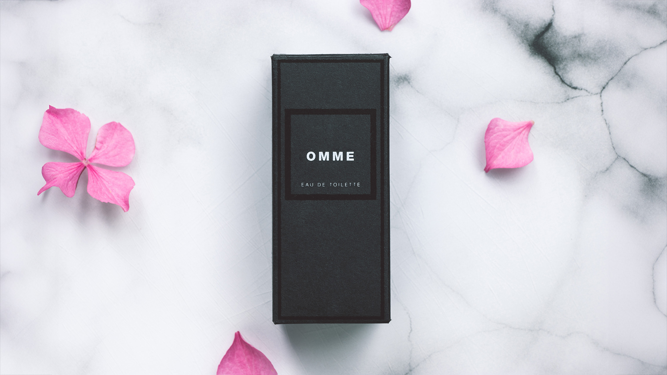 صندوق أسود أنيق مكتوب عليه "OMME Eau de Toilette" محاط ببتلات وردية رقيقة على سطح رخامي