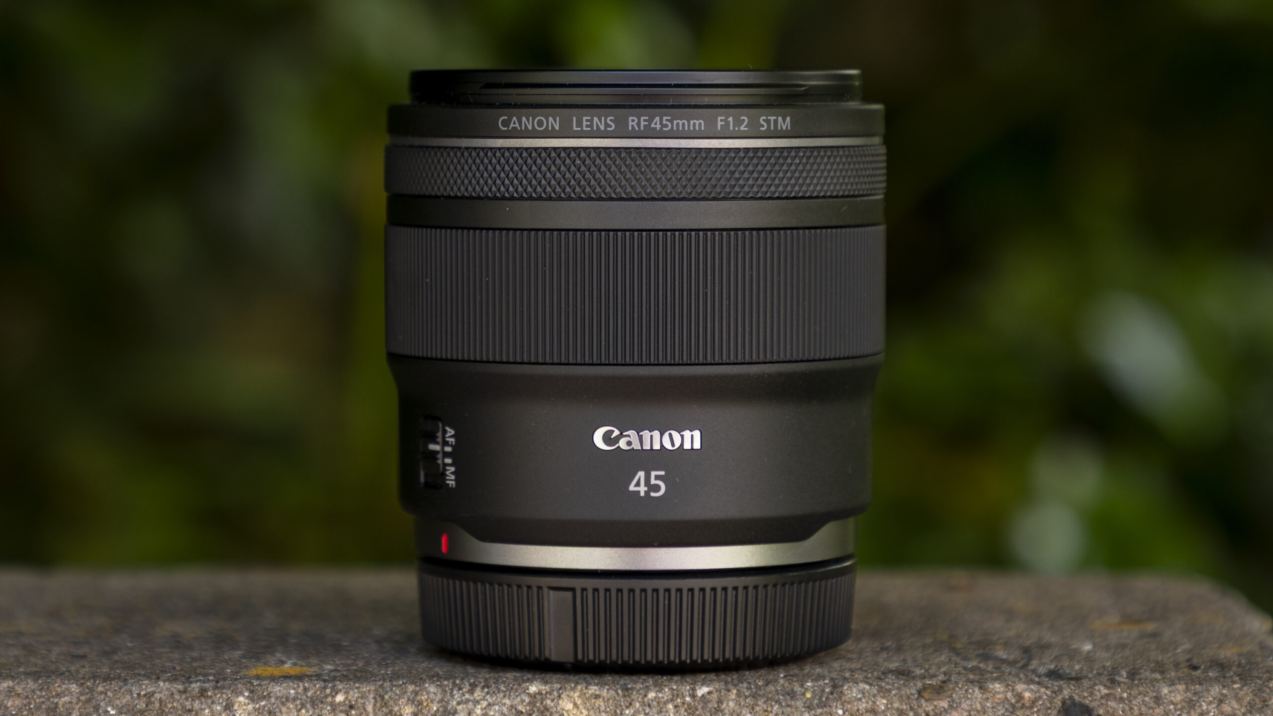عدسة Canon RF 45mm F1.2 STM على جدار مع خلفية خضراء ضبابية