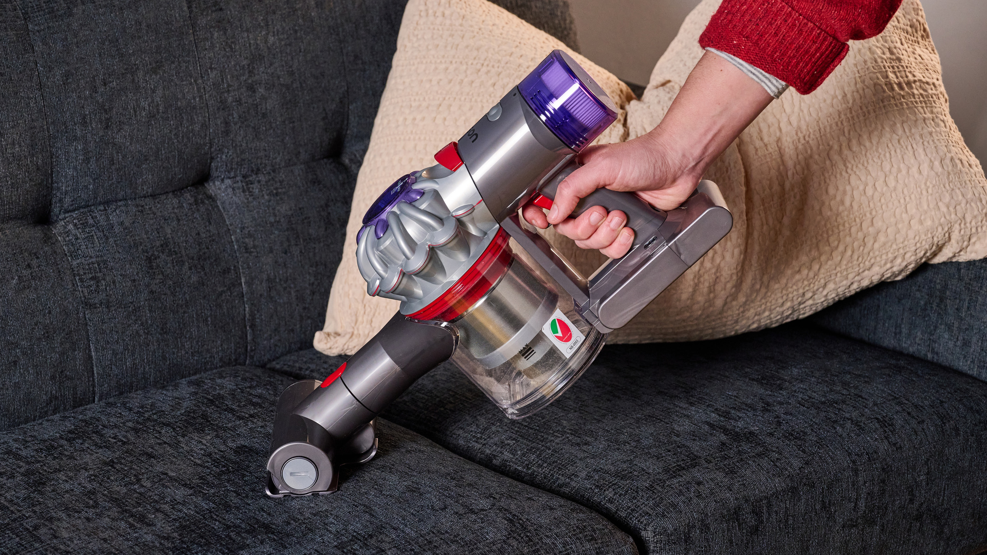 Eine Person, die einen Dyson Car+Boat Handstaubsauger auf einem Sofa benutzt