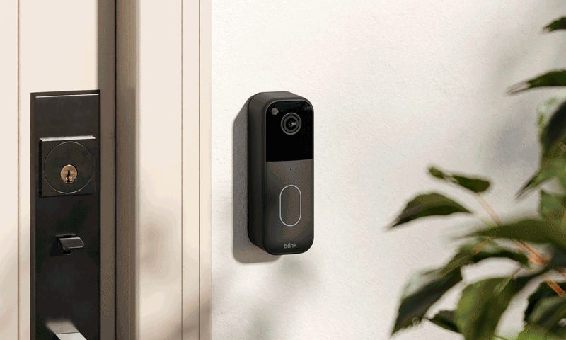 Het Blink Video Doorbell-model uit 2023 is gemonteerd op een witte muur naast een voordeur.