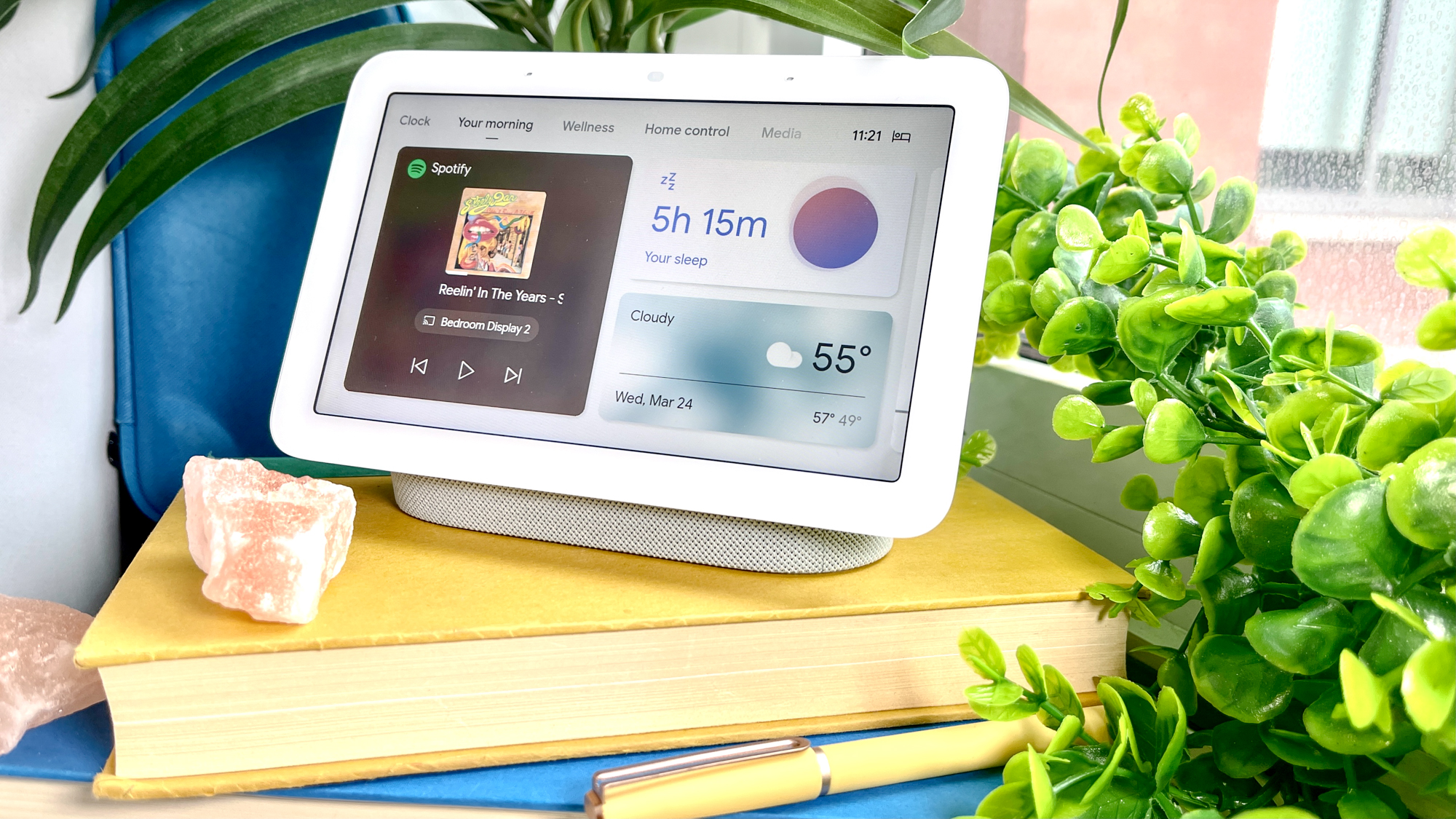 جهاز Google Nest Hub (الجيل الثاني) على كومة كتب بجانب نافذة محاطة بنباتات منزلية