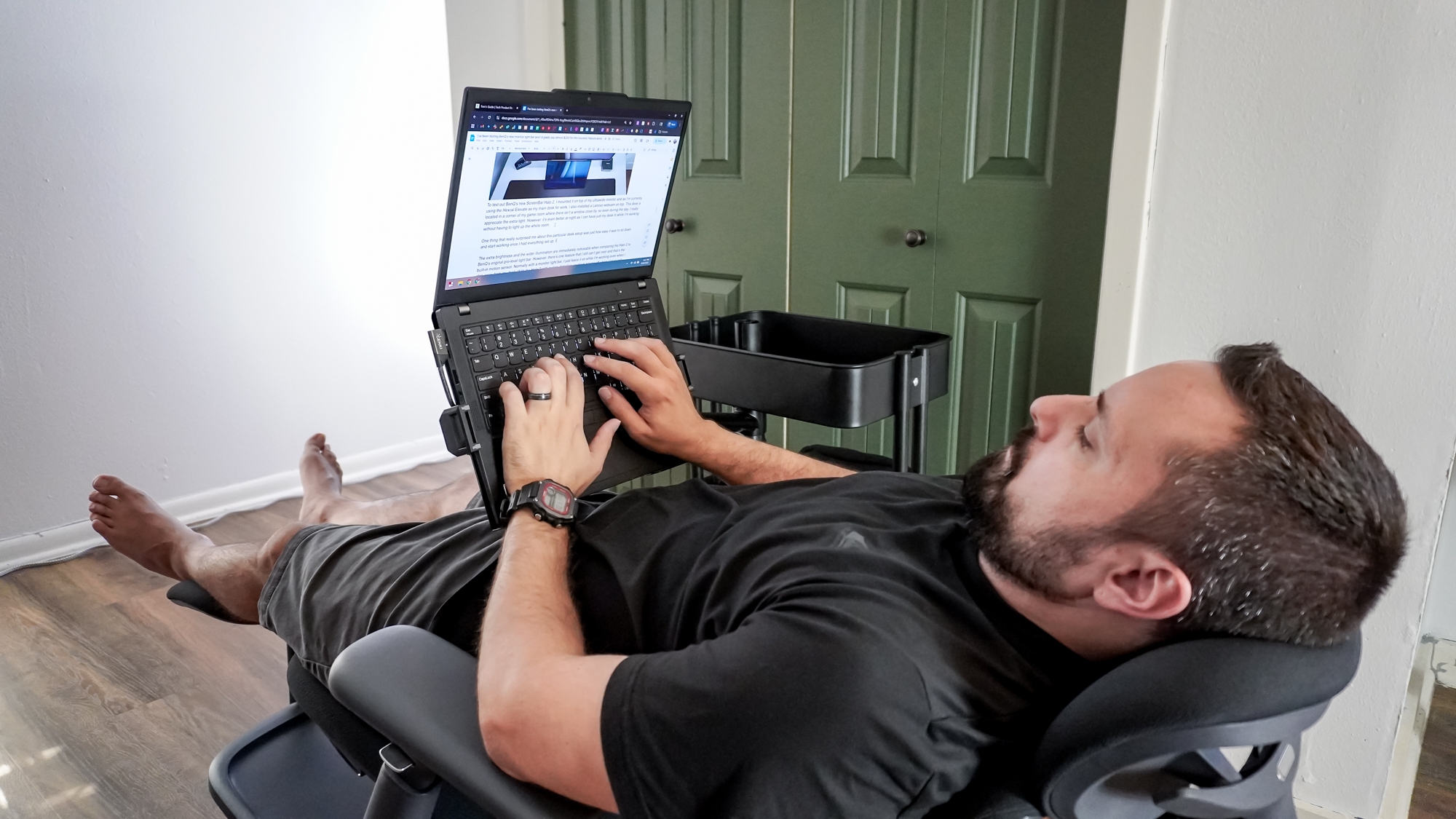 Una persona lavora al computer portatile presso una postazione di lavoro mobile autocostruita, seduta su una poltrona da ufficio completamente reclinabile con i piedi appoggiati su un poggiapiedi indipendente.