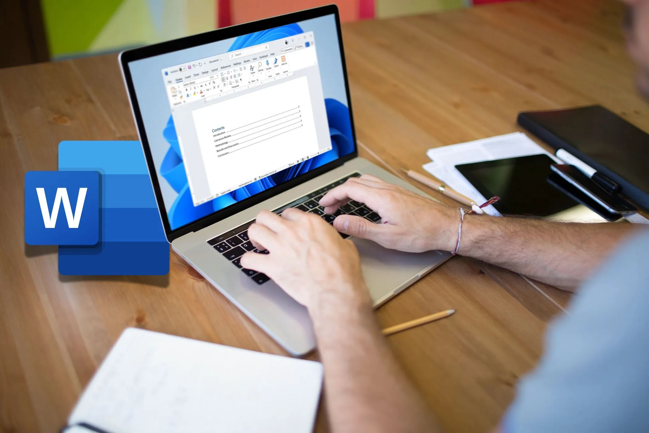 Person using Microsoft Word laptop on a desk with Word icon on the left
