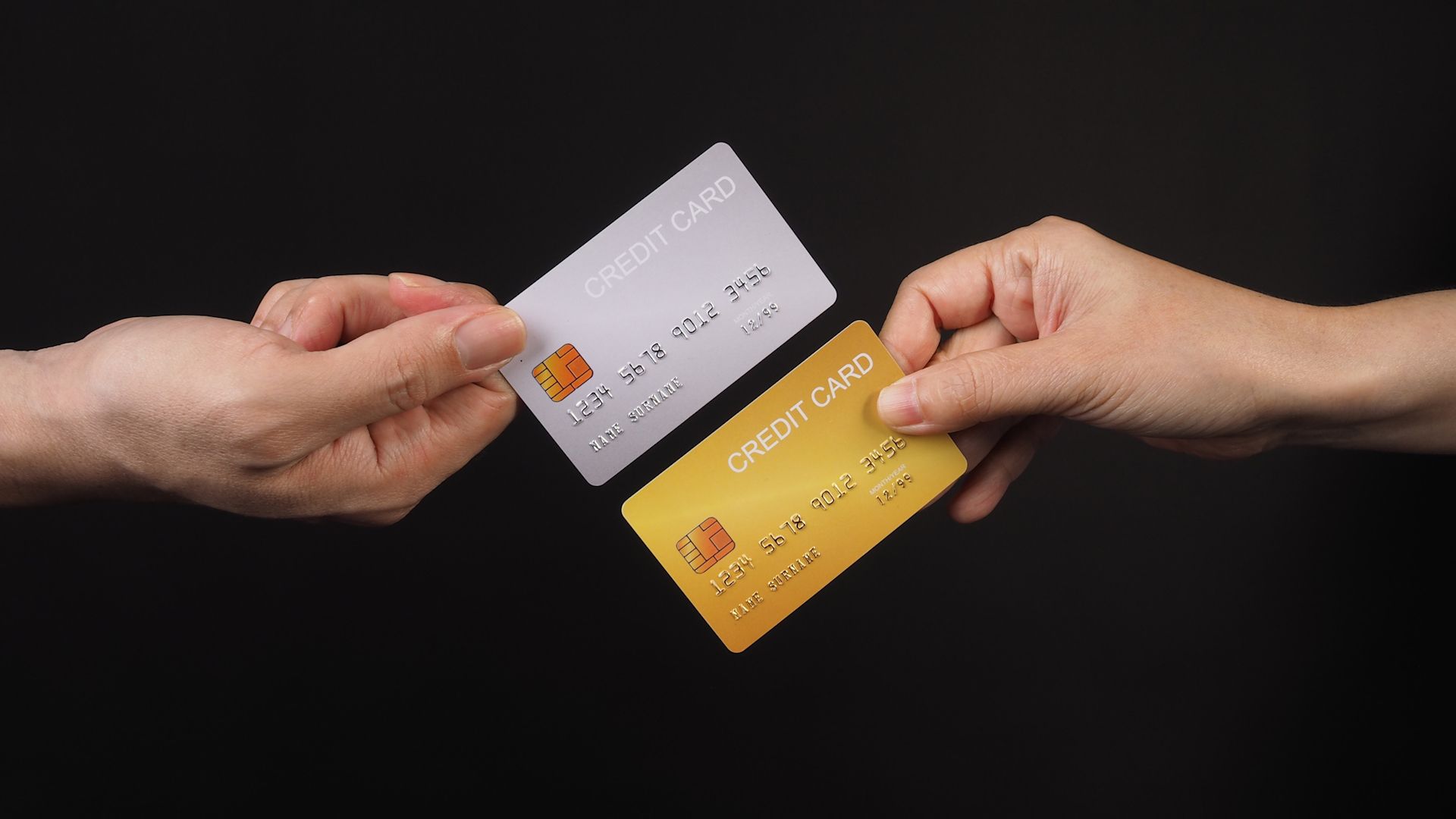 two hands holding credit cards with black background.