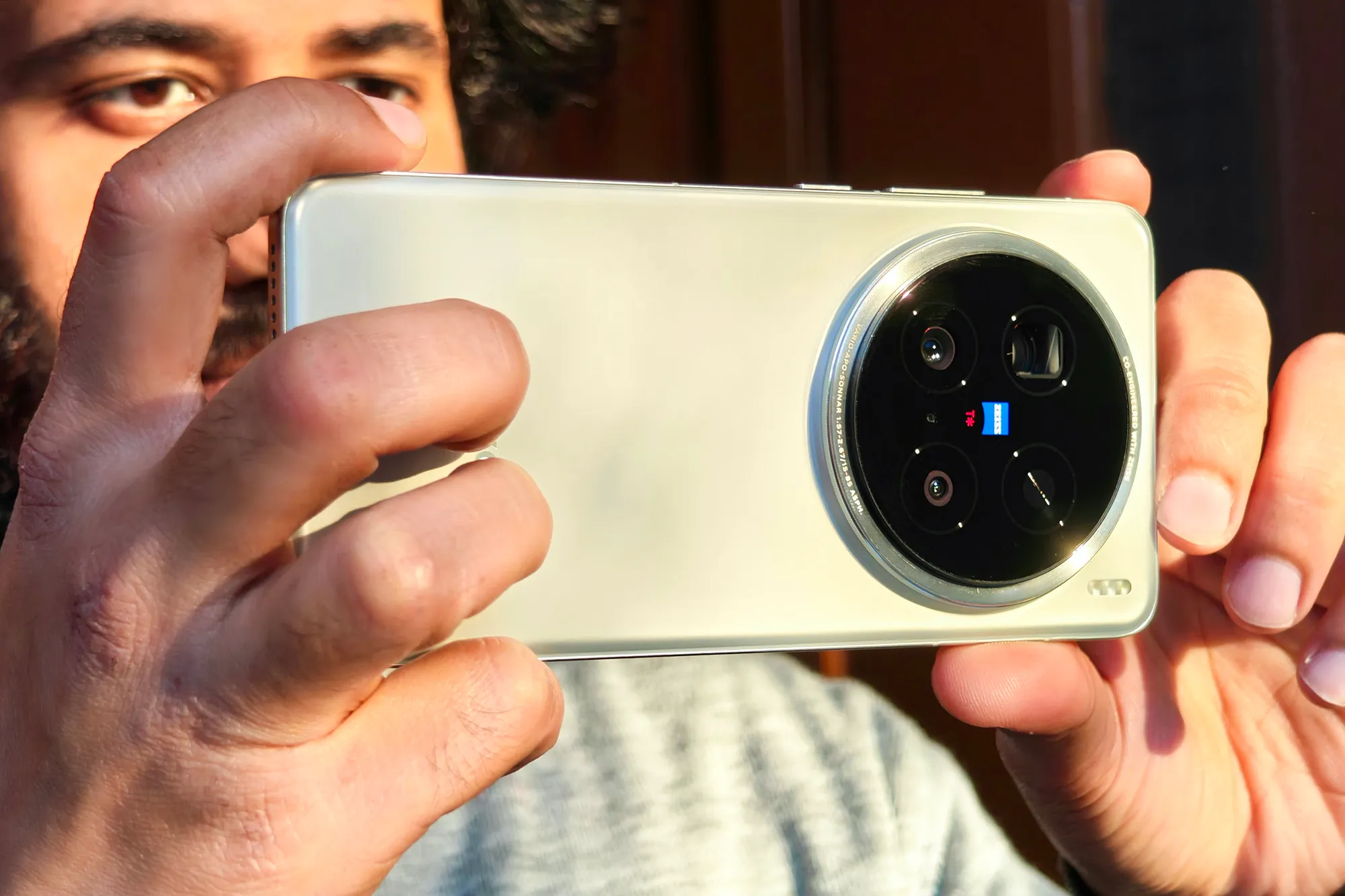 Man holding Vivo X200 Pro with Zeiss lenses up to his face.