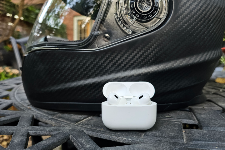 Apple AirPods Pro 2 sitting in front of a motorcycle helmet.
