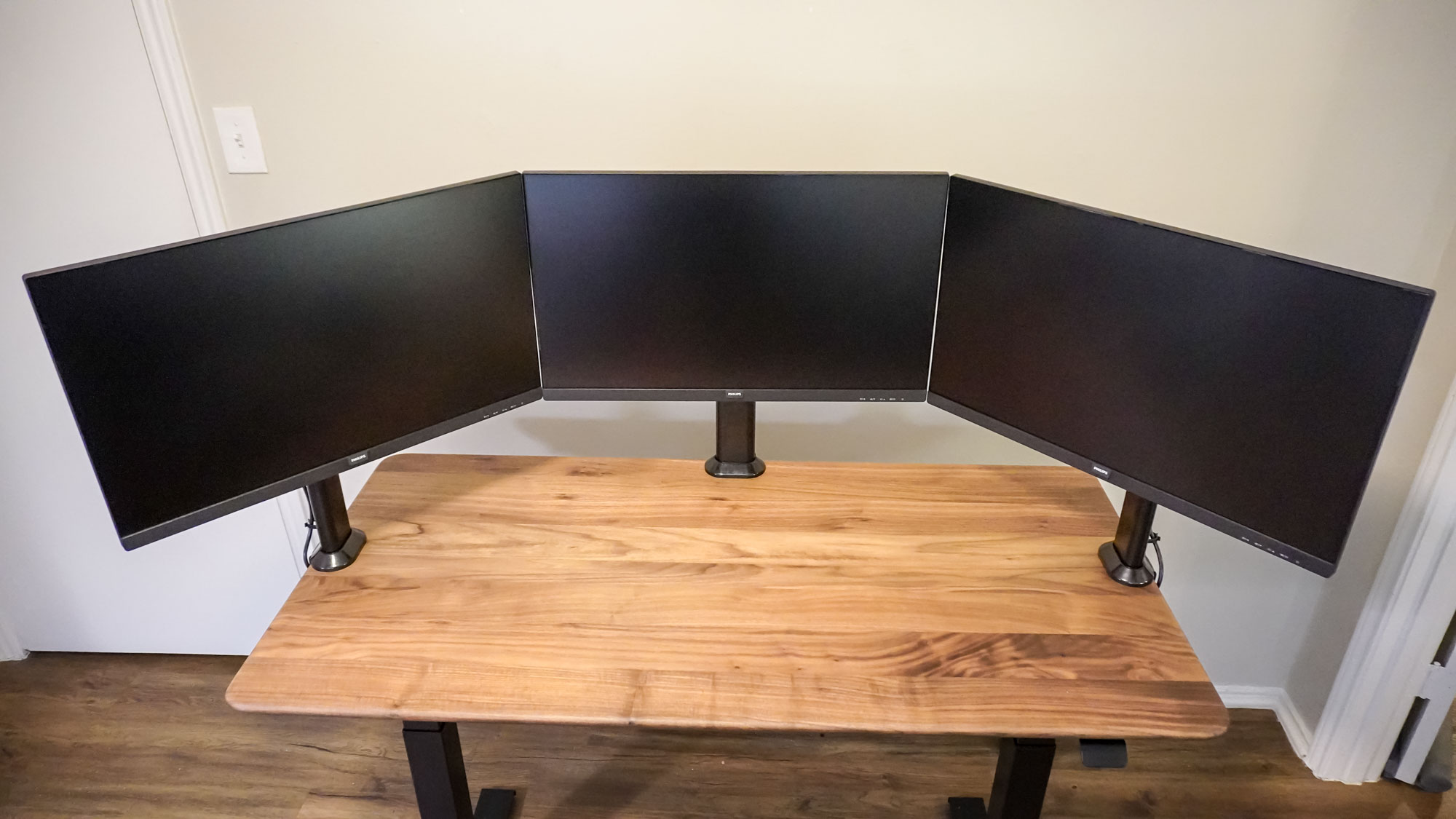 Three identical monitors mounted to a desk arranged in a triple monitor setup configuration