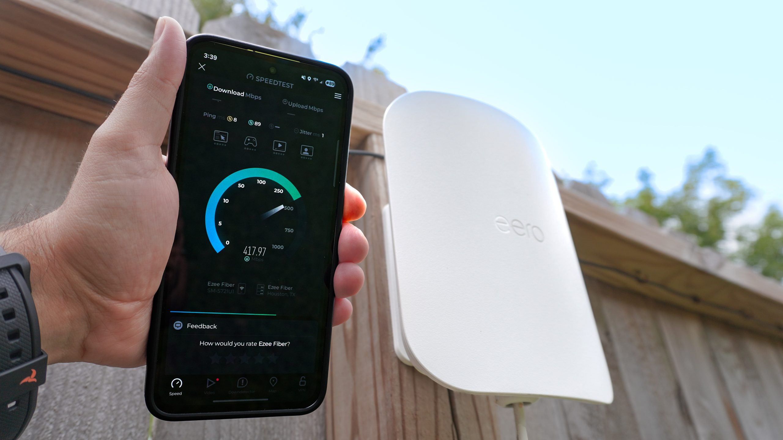 شخص يحمل هاتفًا يجري اختبار سرعة الإنترنت وفي الخلفية موسع شبكة eero Outdoor 7 مثبت على سياج