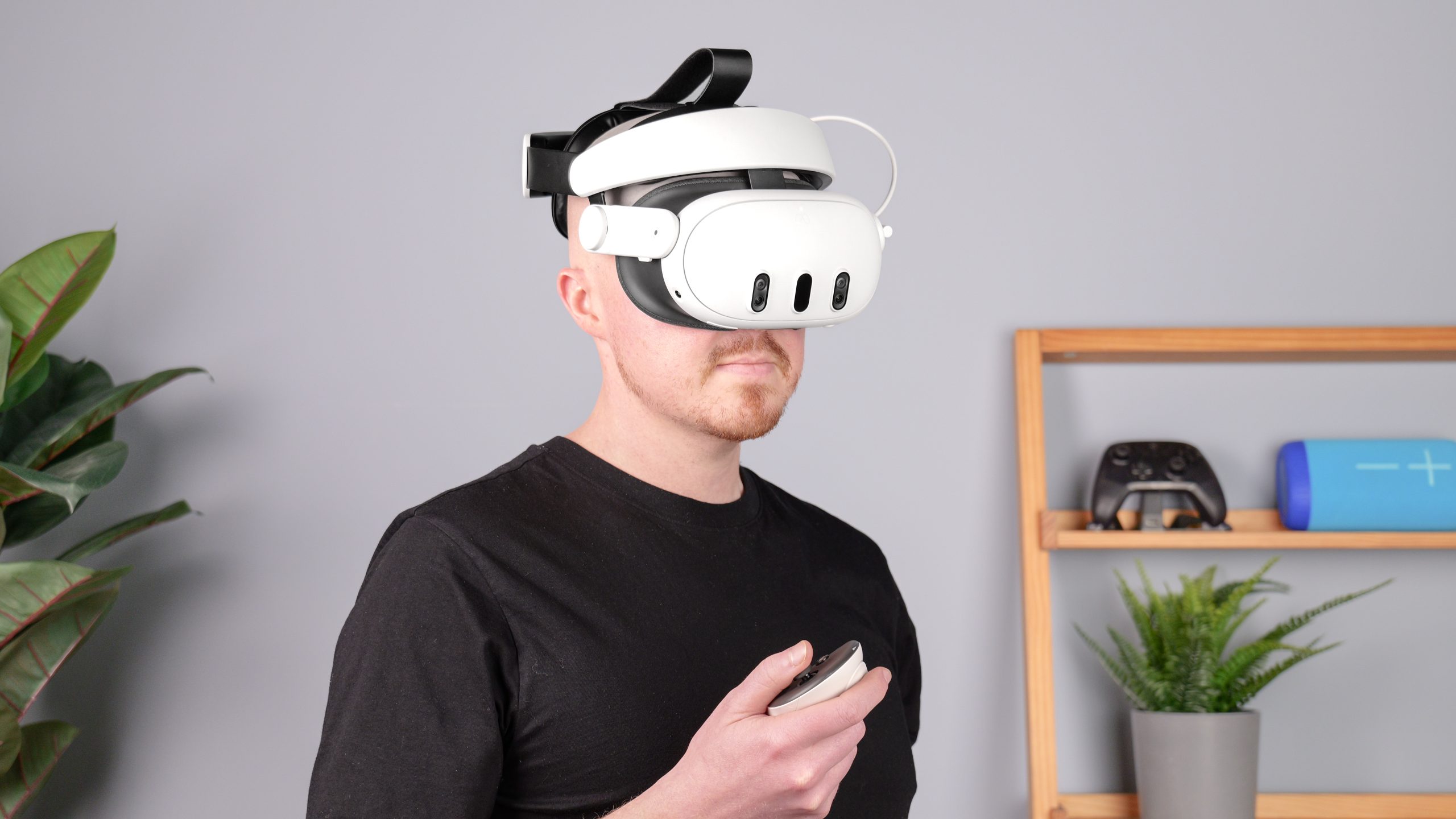 Kiwi Design H4 Boost Halo Battery Strap with Meta Quest 3 on person holding controller and plant and shelf in background