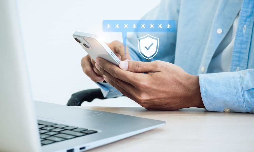 مفهوم المصادقة الثنائية. أيقونة درع أمان افتراضي أثناء الوصول على الهاتف مع الكمبيوتر المحمول للتحقق من صحة كلمة المرور، والتحقق من الهوية، والأمن السيبراني مع تكنولوجيا المصادقة البيومترية.
