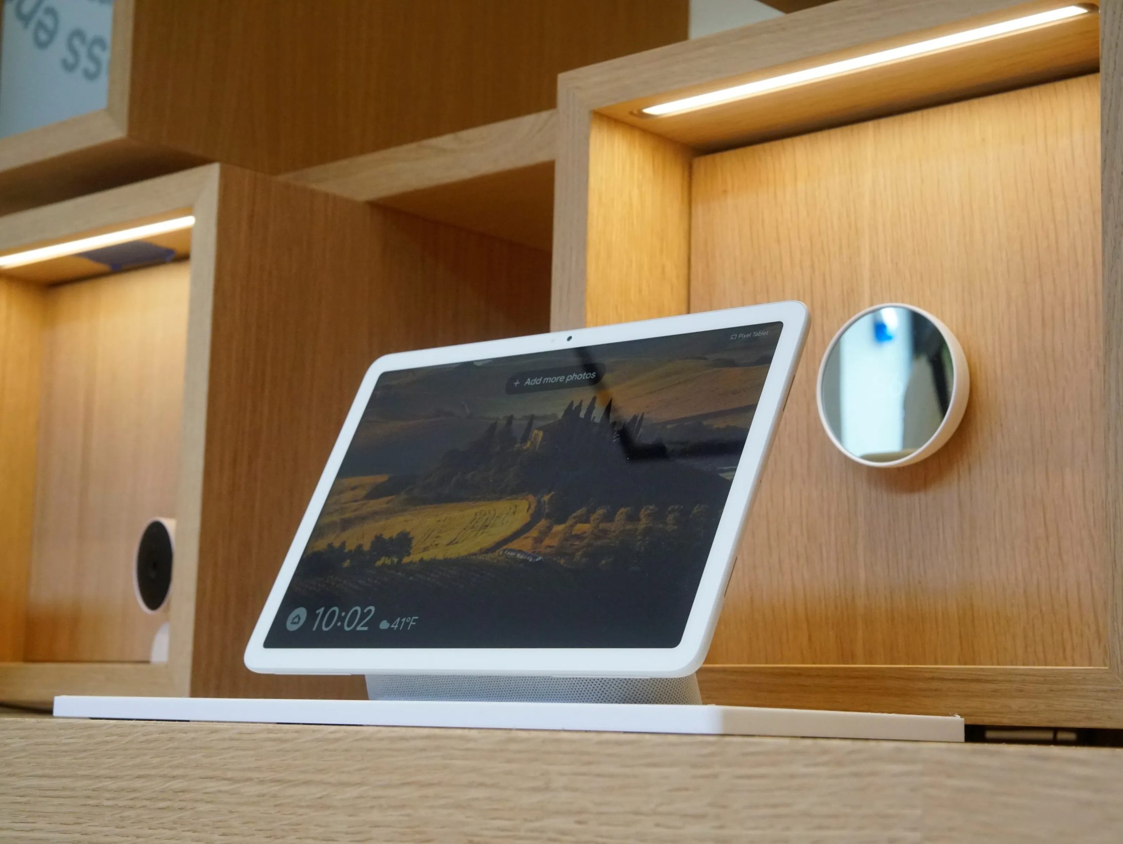 جهاز Pixel Tablet موضوع على طاولة مع ترموستات Nest على الحائط في الخلفية.