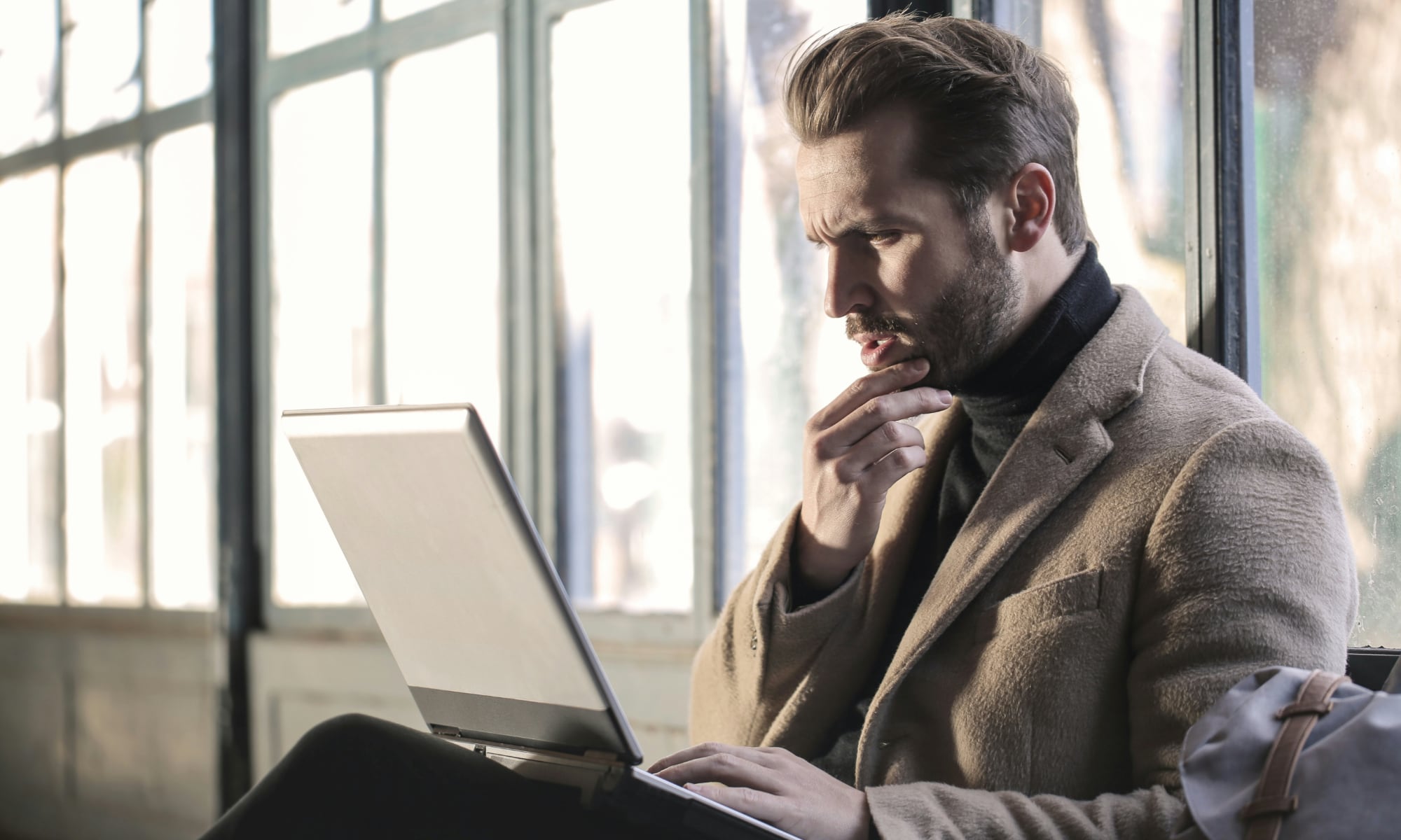 رجل ينظر إلى جهاز كمبيوتر محمول وهو يحك ذقنه في حيرة