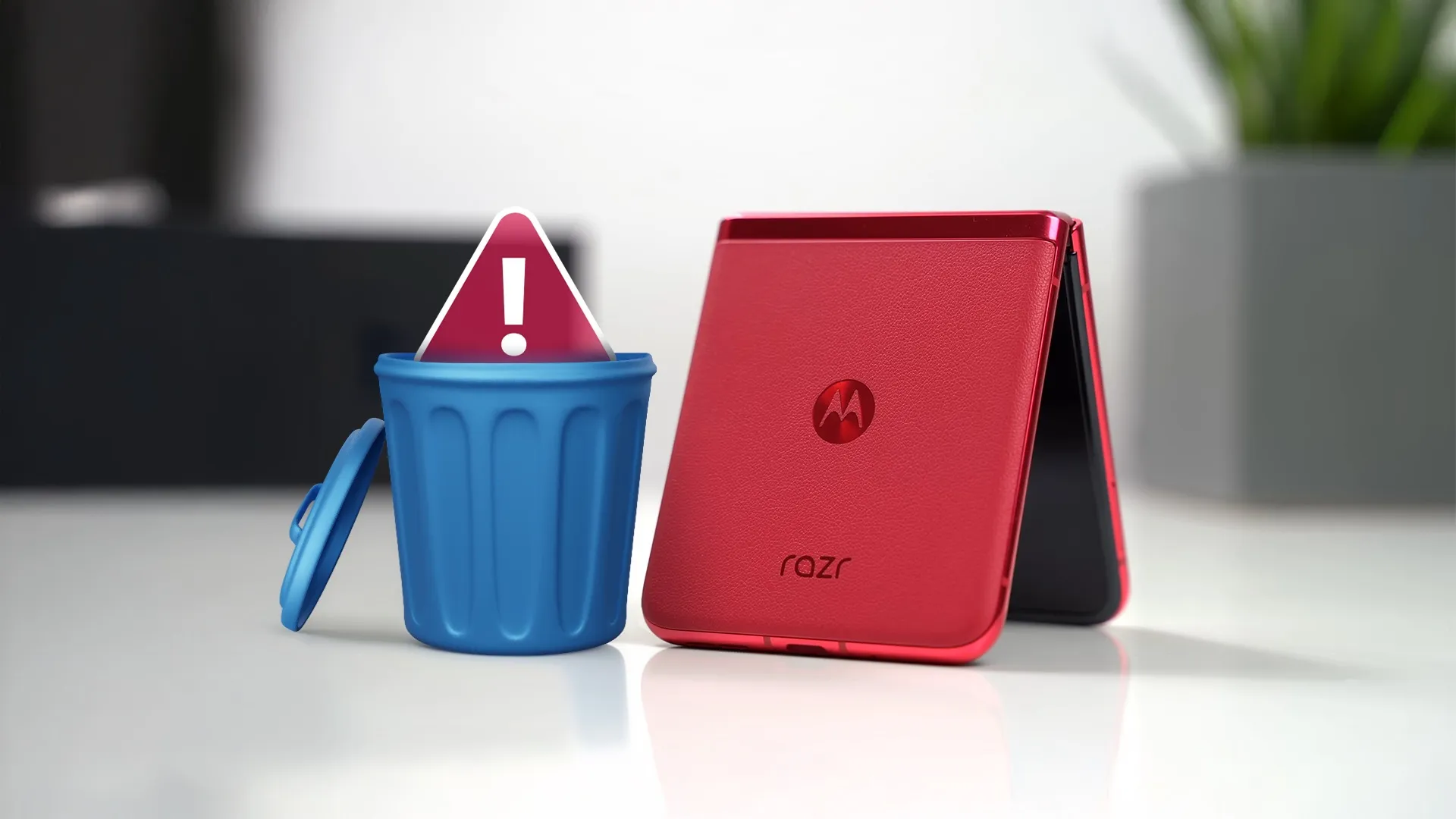 هاتف Motorola أحمر مطوي بجانب سلة مهملات زرقاء صغيرة مع علامة تحذير حمراء بداخلها