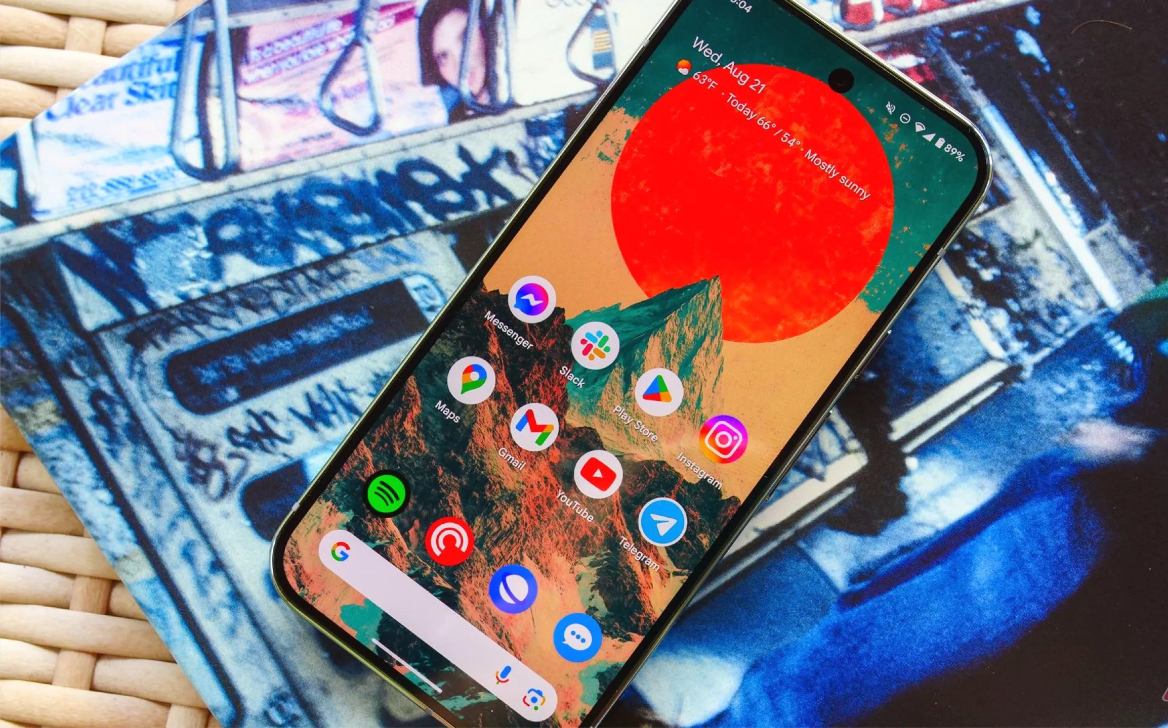 صورة لهاتف Pixel 9 Pro موضوع على طاولة من الخيزران وإلى جانبه غلاف ألبوم، والشاشة مضاءة