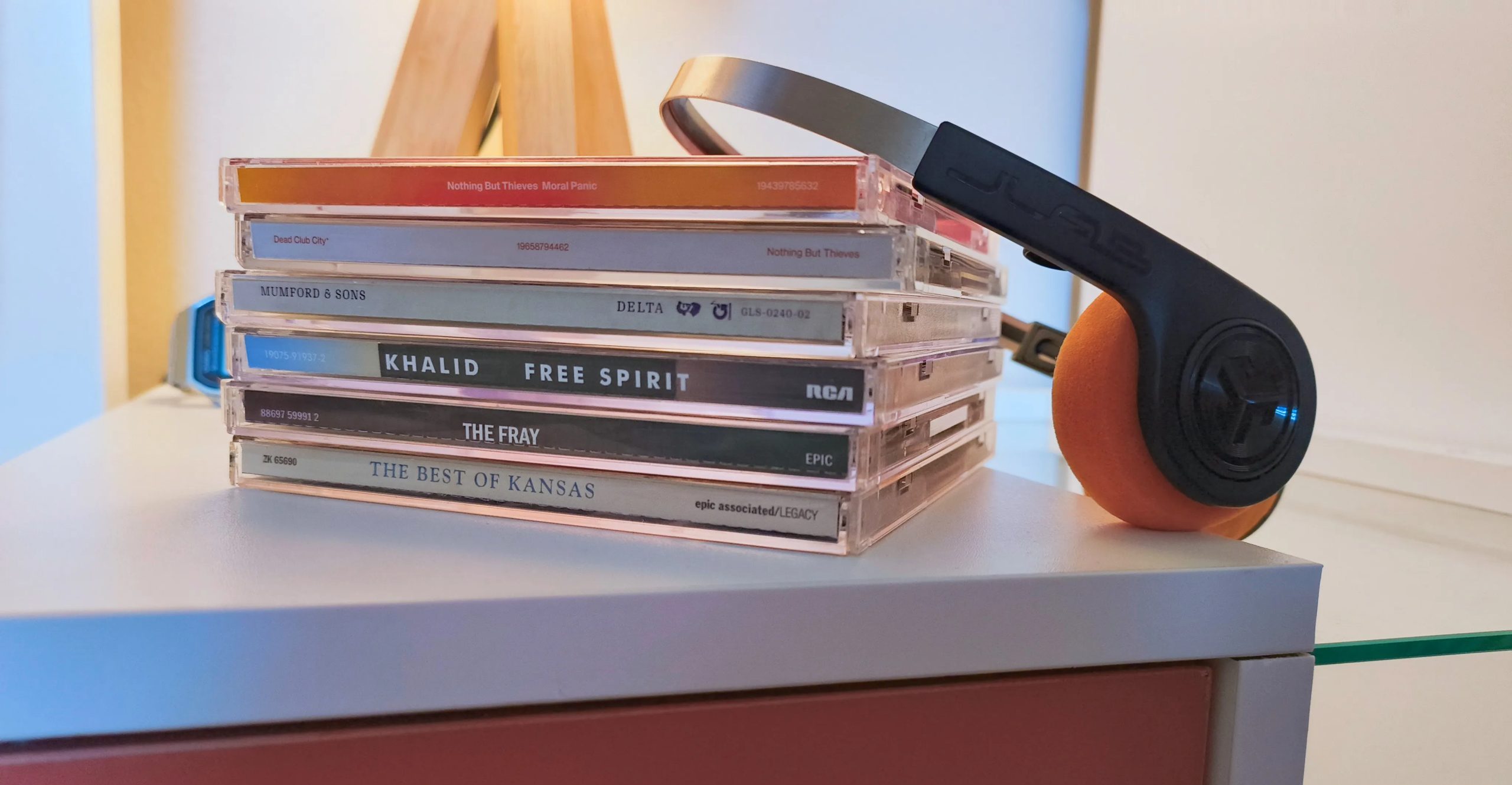 كومة من الأقراص المدمجة وزوج من سماعات الرأس السوداء والبرتقالية على طاولة جانبية بيضاء