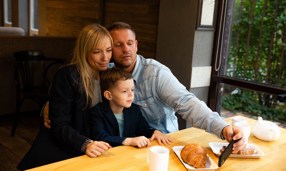 عائلة سعيدة تتناول الإفطار في المخبز، تستمتع بالحلويات وتلتقط صورة سيلفي، لحظة عائلية دافئة في مشهد المقهى. مفهوم الترابط العائلي، لحظات الفرح، رعاية الأسرة