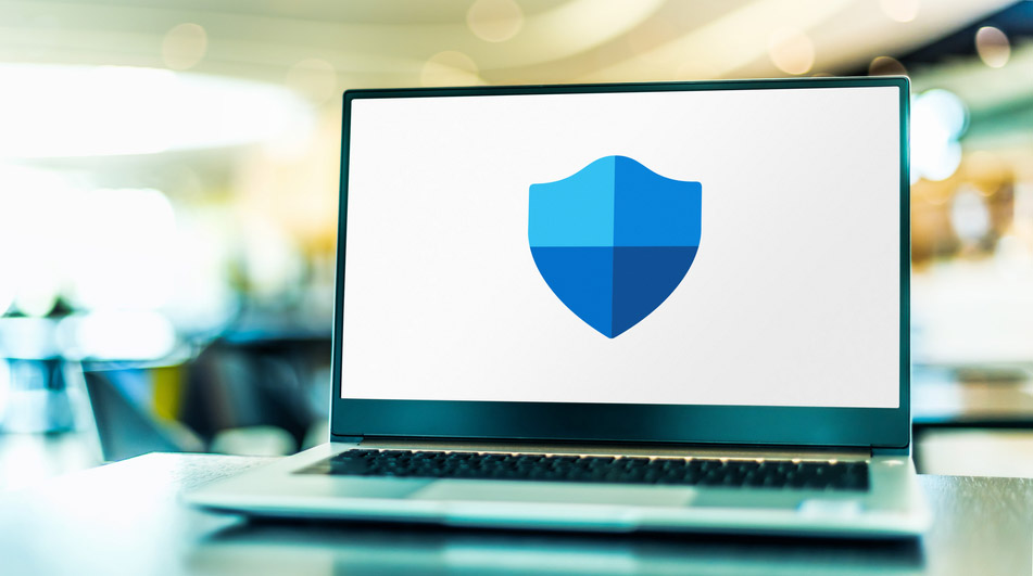 شعار برنامج Microsoft Defender Antivirus، المعروف أيضًا باسم Windows Defender، معروض على شاشة جهاز لابتوب موضوع على طاولة.