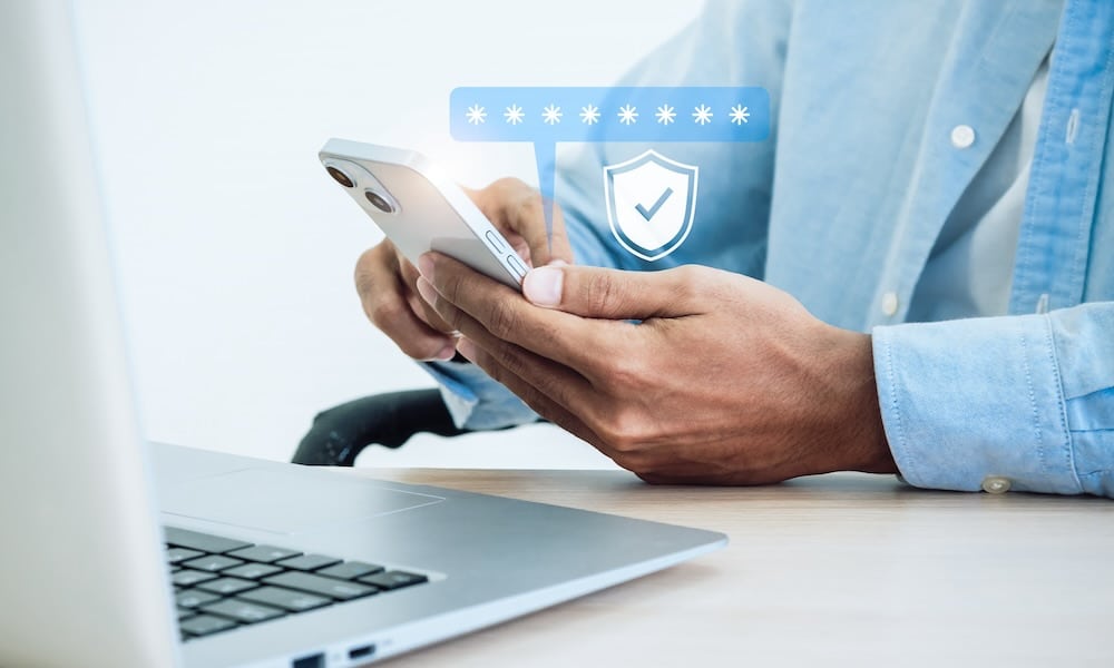 مفهوم المصادقة الثنائية. أيقونة درع أمان افتراضي أثناء الوصول على الهاتف مع الكمبيوتر المحمول للتحقق من صحة كلمة المرور، والتحقق من الهوية، والأمن السيبراني مع تقنية المصادقة البيومترية.
