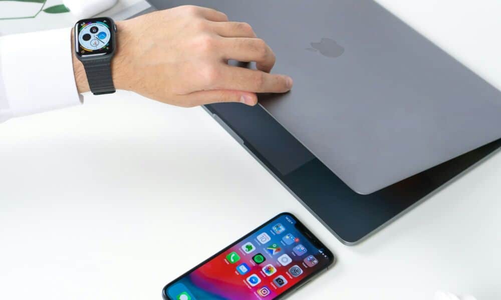 شخص يفتح جهاز MacBook ويرتدي ساعة Apple Watch مع iPhone