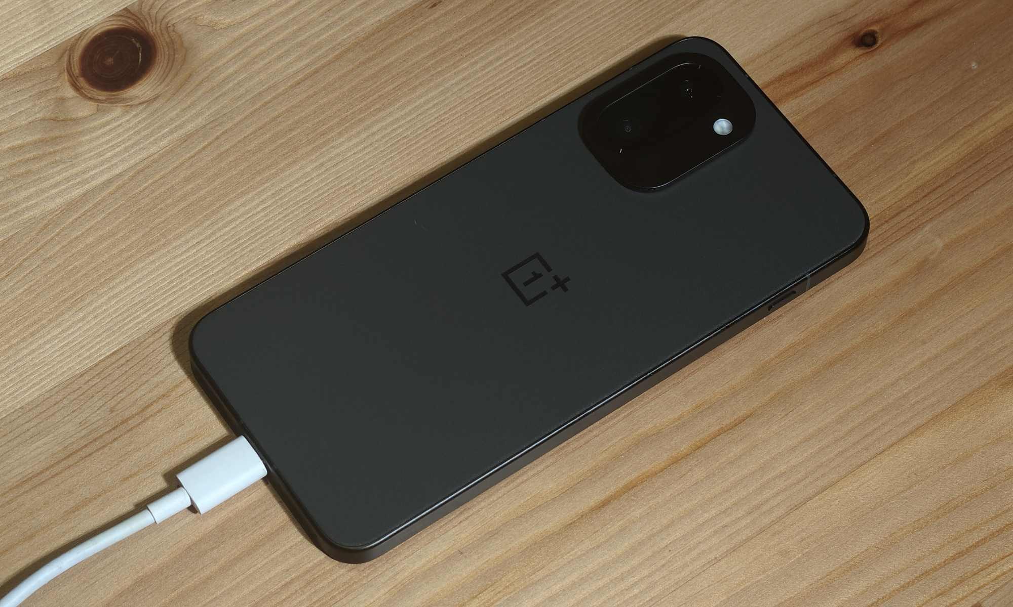 هاتف OnePlus 15R مسطح على طاولة، مع توصيل كابل شحن.