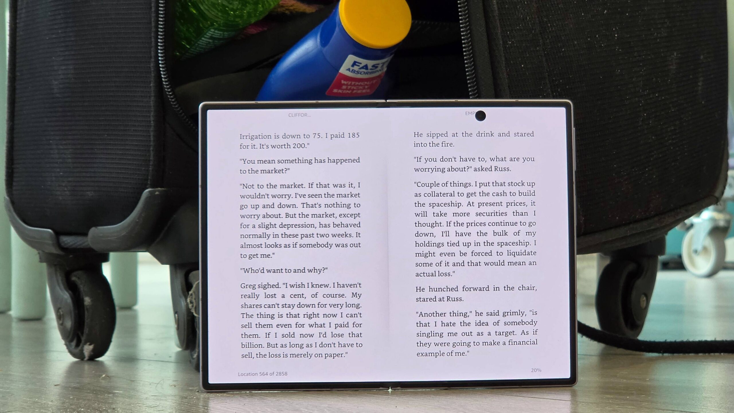 هاتف Samsung Galaxy Z Fold 8 يعرض تطبيق Kindle، بجانب حقيبة سفر تتسرب محتوياتها.