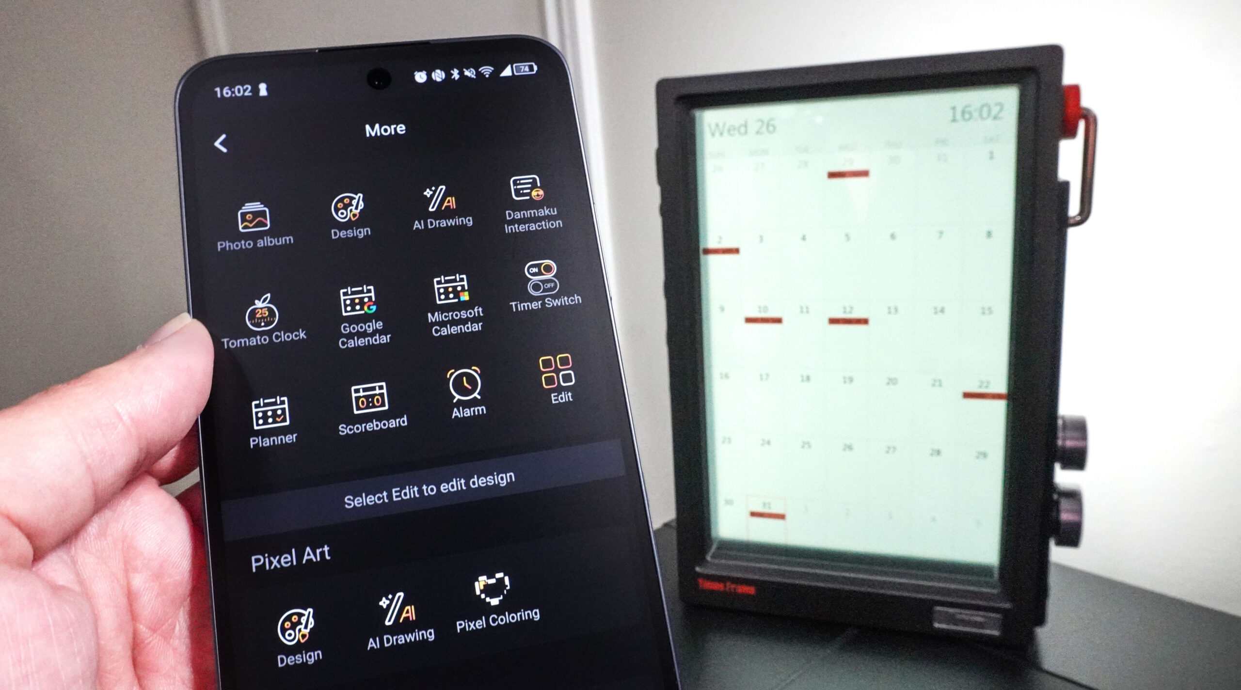 جهاز Divoom Times Frame يعرض تقويمًا في الخلفية مع شخص يمسك هاتفًا يُظهر تكاملات التقويم في تطبيق Divoom