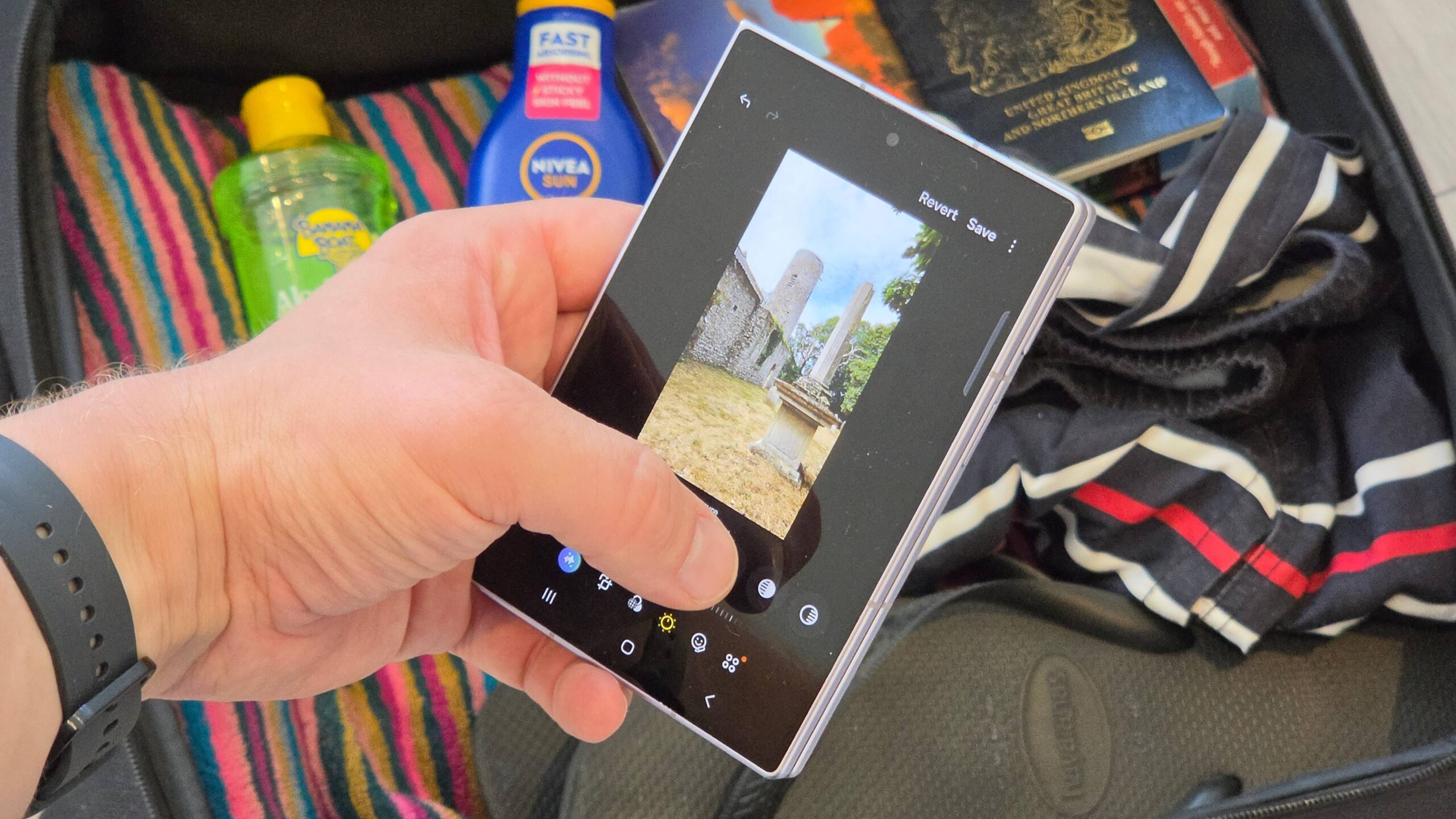 هاتف Samsung Galaxy Z Fold 8 يعرض صفحة تحرير الصور، فوق حقيبة سفر معبأة.