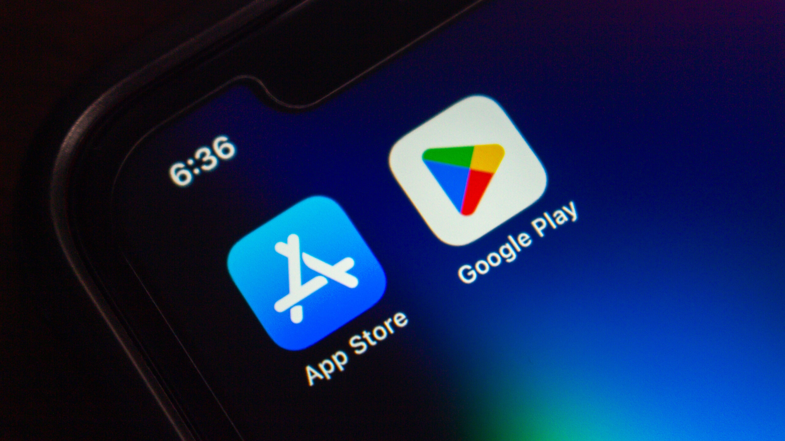 لقطة مقربة لشاشة هاتف ذكي تعرض أيقونتي App Store و Google Play جنبًا إلى جنب على خلفية داكنة.