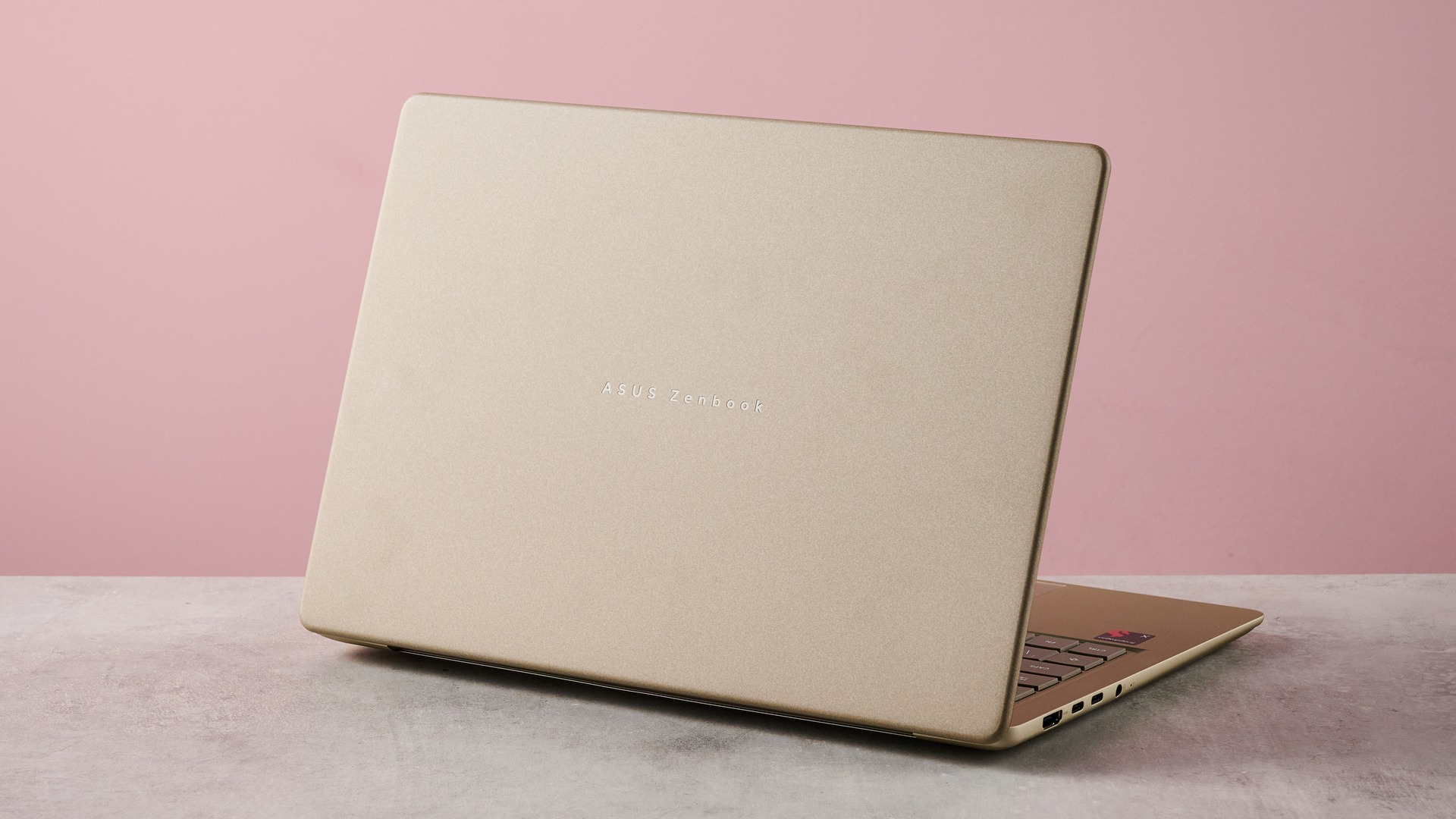 منظر خلفي ثلاثي الأرباع لجهاز Asus Zenbook 14 2026 على مكتب بخلفية جدار وردي