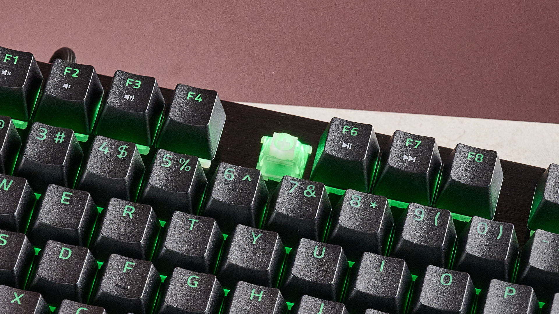 لقطة مقربة للصف العلوي من مفاتيح لوحة المفاتيح Razer Huntsman V3 HE Magnetic Tenkeyless 8KHz مع إزالة غطاء مفتاح F5، على مكتب بخلفية جدار وردي