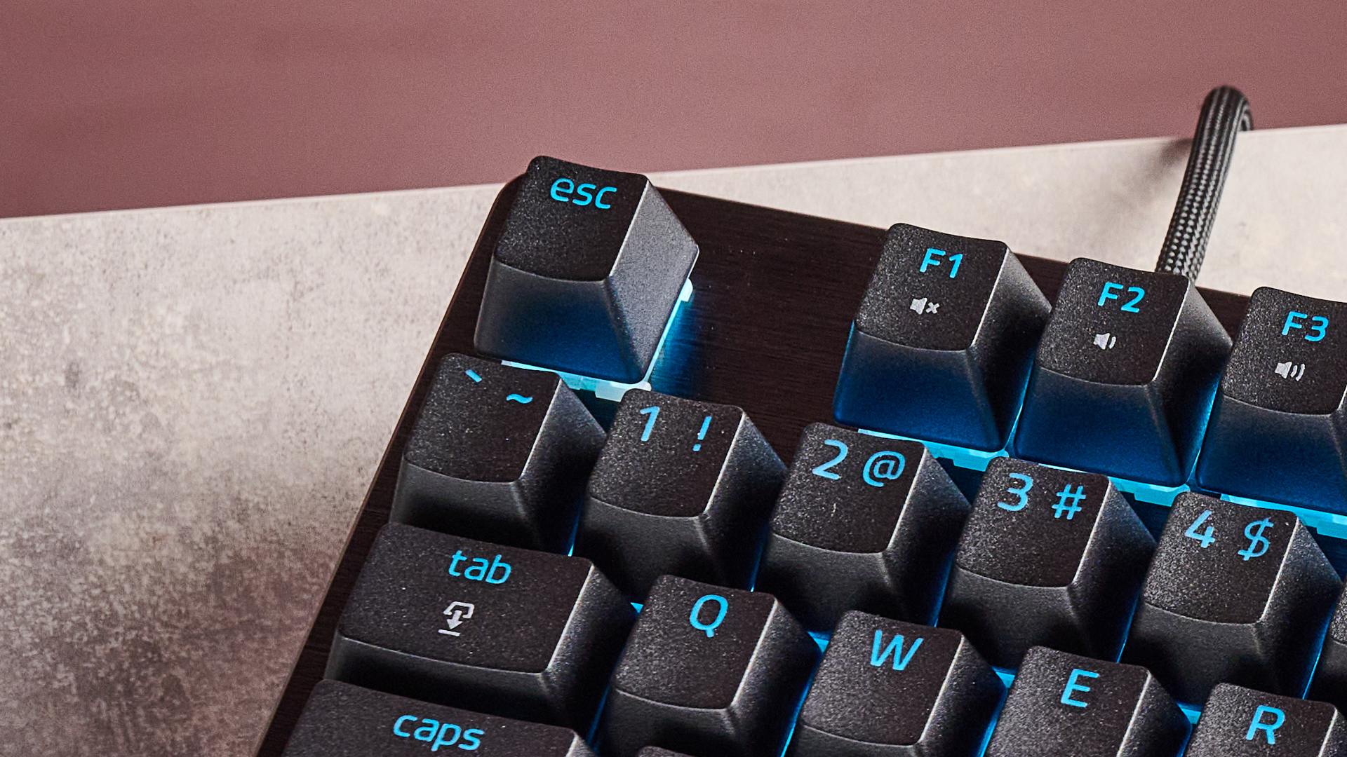 لقطة مقربة لمفتاح الهروب (Escape) على لوحة مفاتيح Razer Huntsman V3 HE Magnetic Tenkeyless 8KHz، على مكتب بخلفية جدار وردي